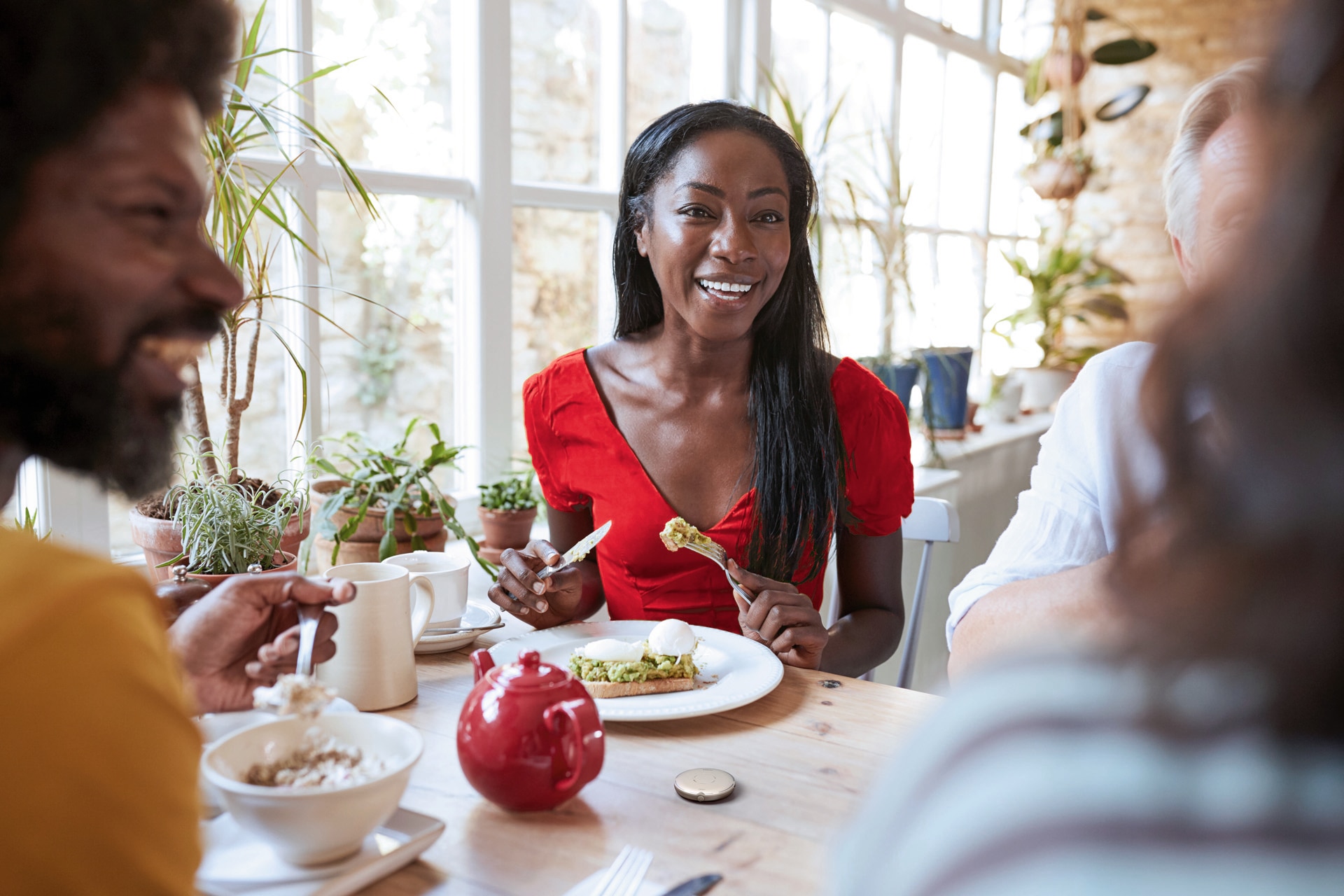 Junge Frau mit Hörsystem bei einer gesunden Mahlzeit unterhält sich fröhlich mit den Anderen an ihrem Tisch. Roger Select liegt vor ihr.