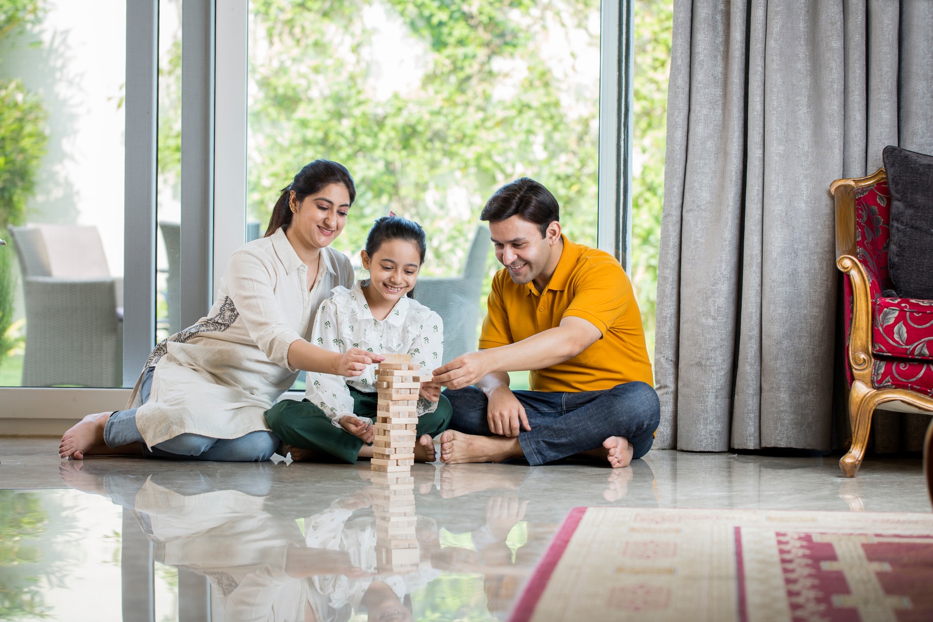 Fröhliche Familie sitzt zu Hause auf dem Boden und spielt mit Holzklötzen.