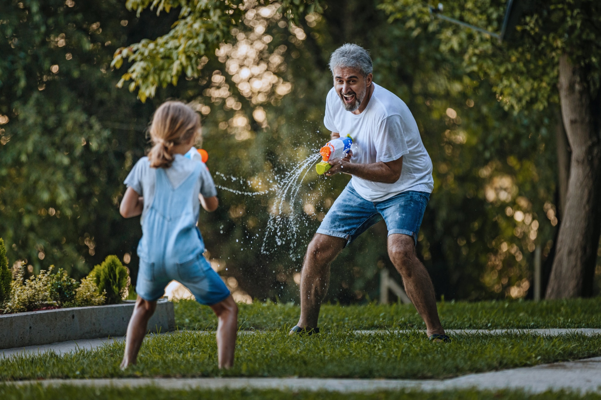Enkelin und Großvater schießen sich im Garten gegenseitig mit Wasserpistolen ab.
