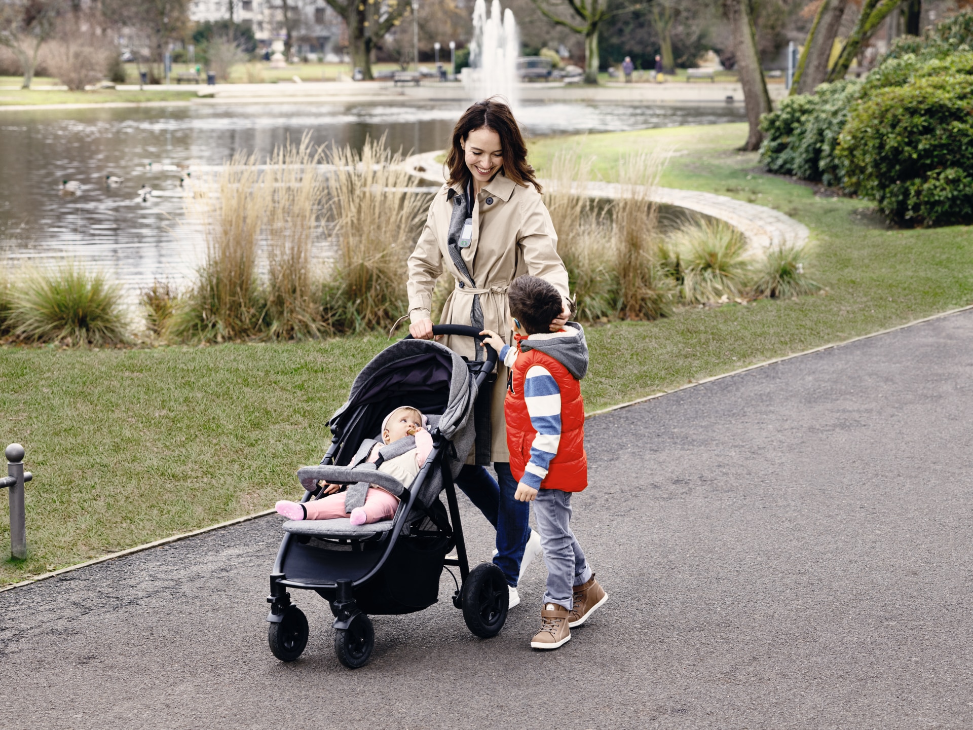 Giovane madre in un parco con i suoi due figli, uno dei quali porta un apparecchio acustico.