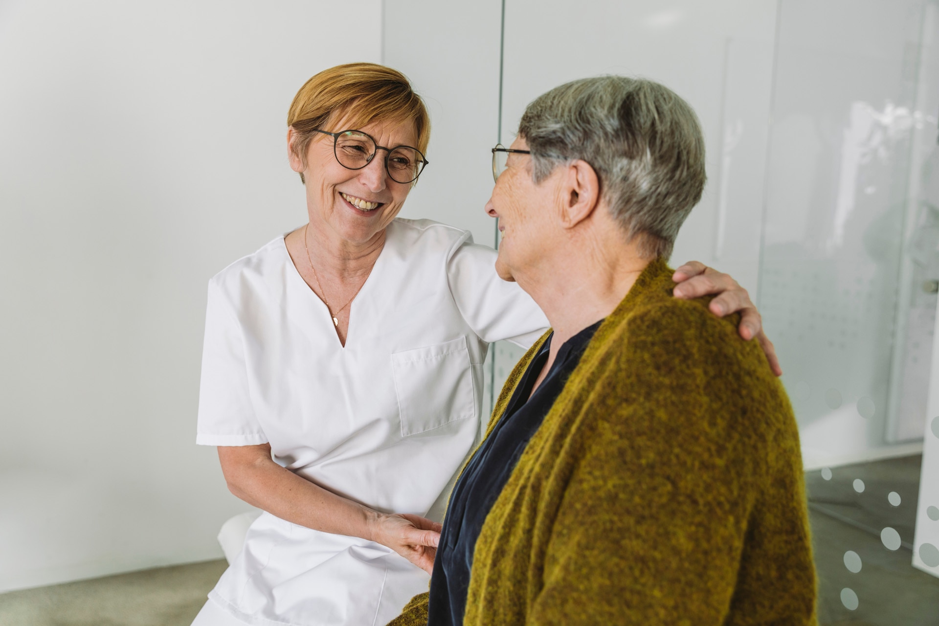 Legeassistent oppmuntrer eldre pasient på legekontor.