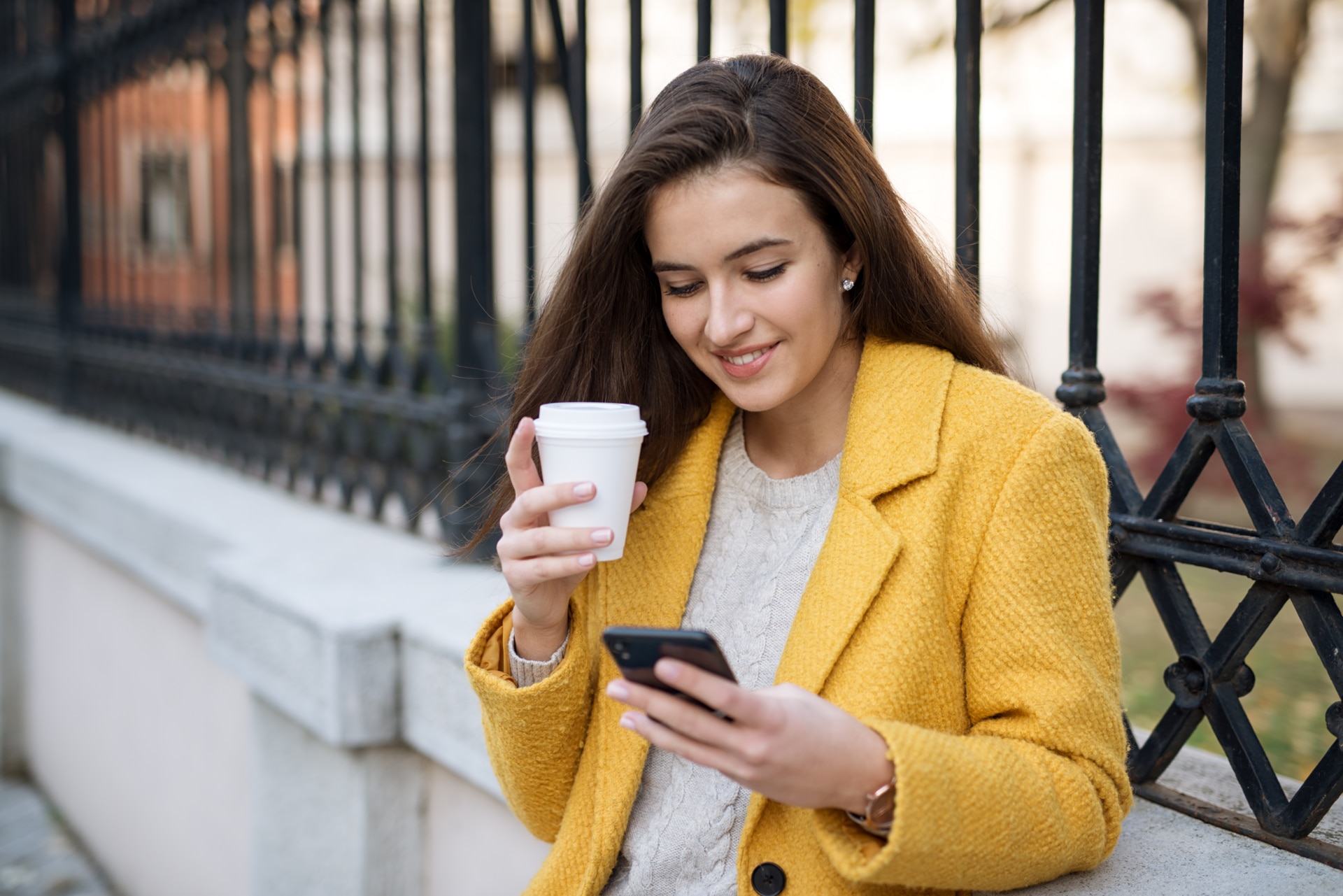 Smilende kvinne bruker mobilen og drikker kaffe