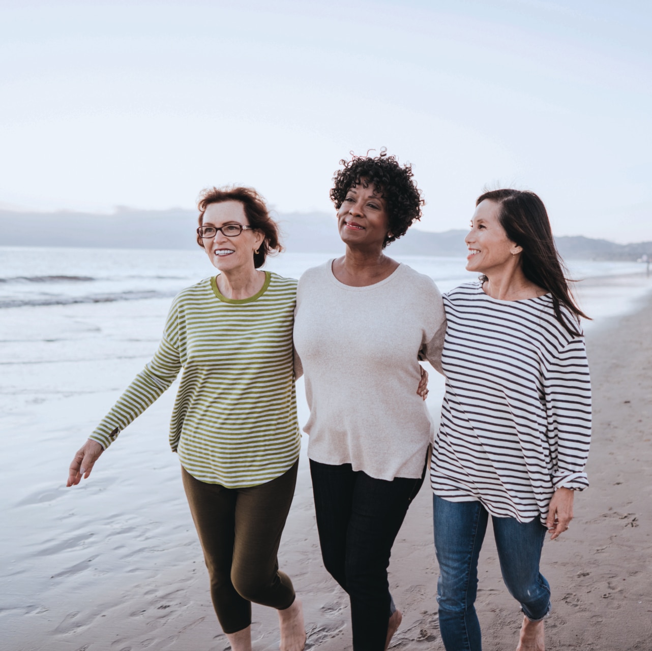 Three friends walking on the beach, appearing to be happy.