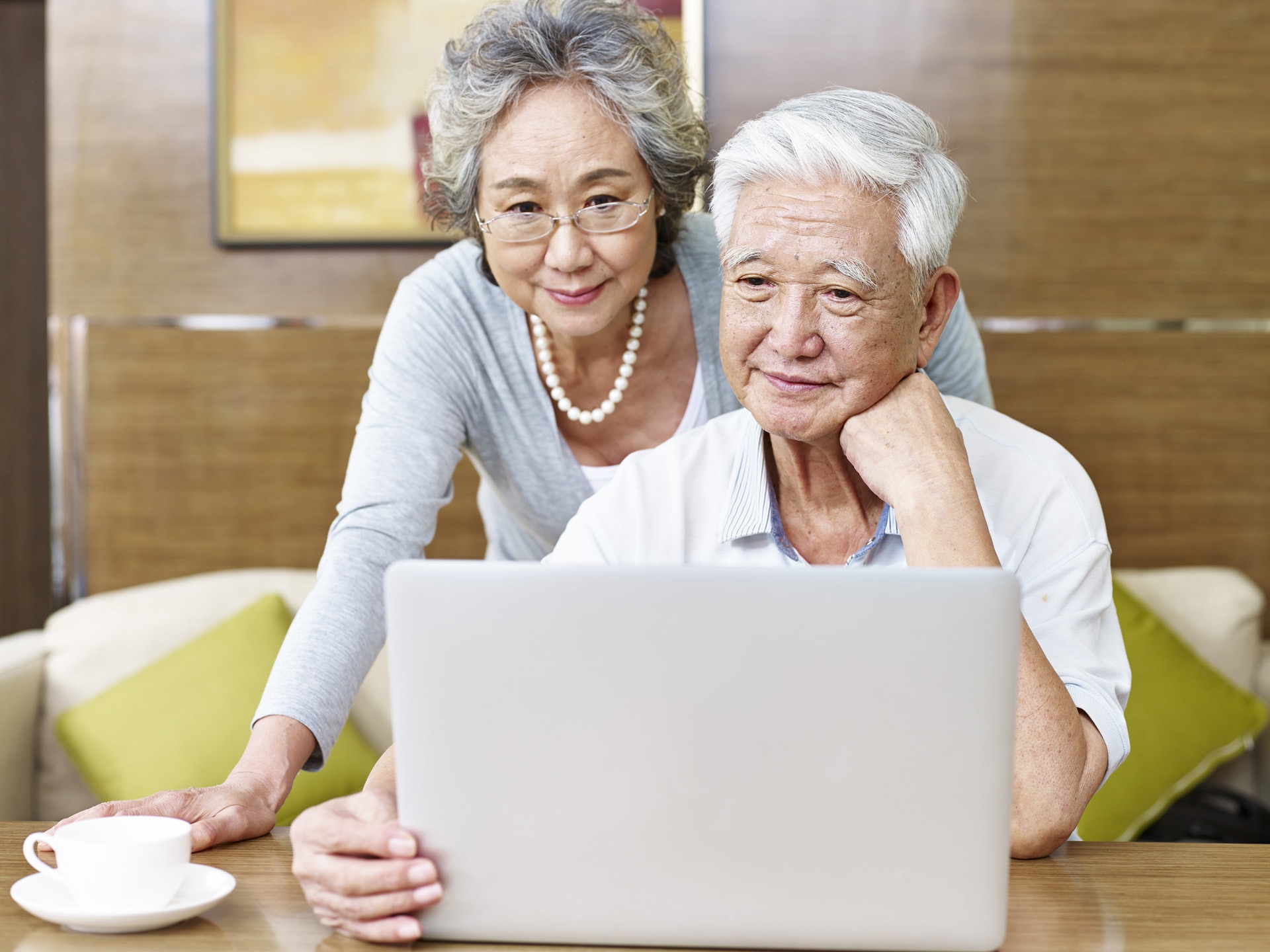Verliebtes älteres asiatisches Paar sitzt gemeinsam vor einem Laptop;