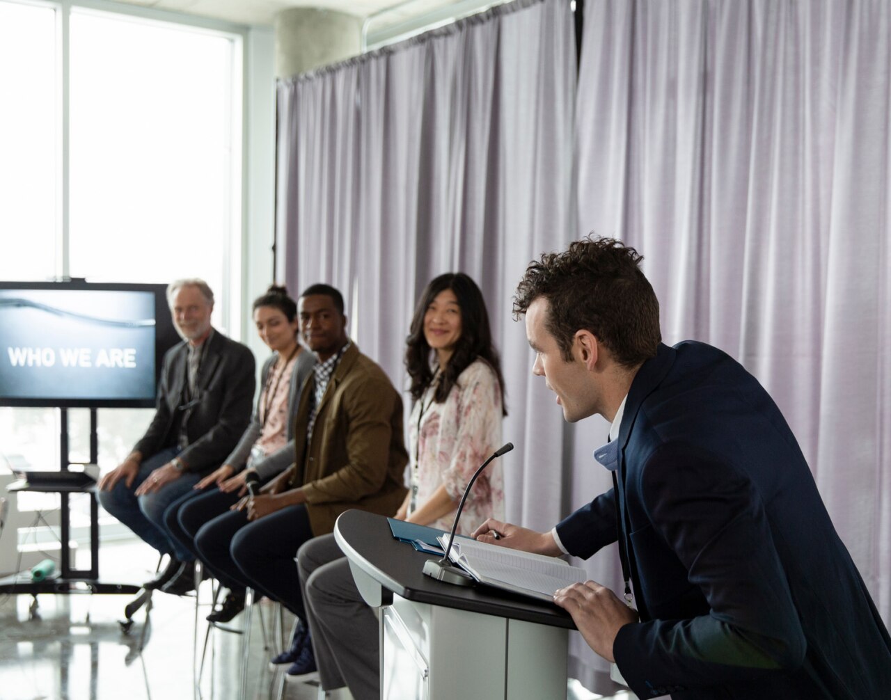 Man at podium introducing panel of motivation speakers at conference