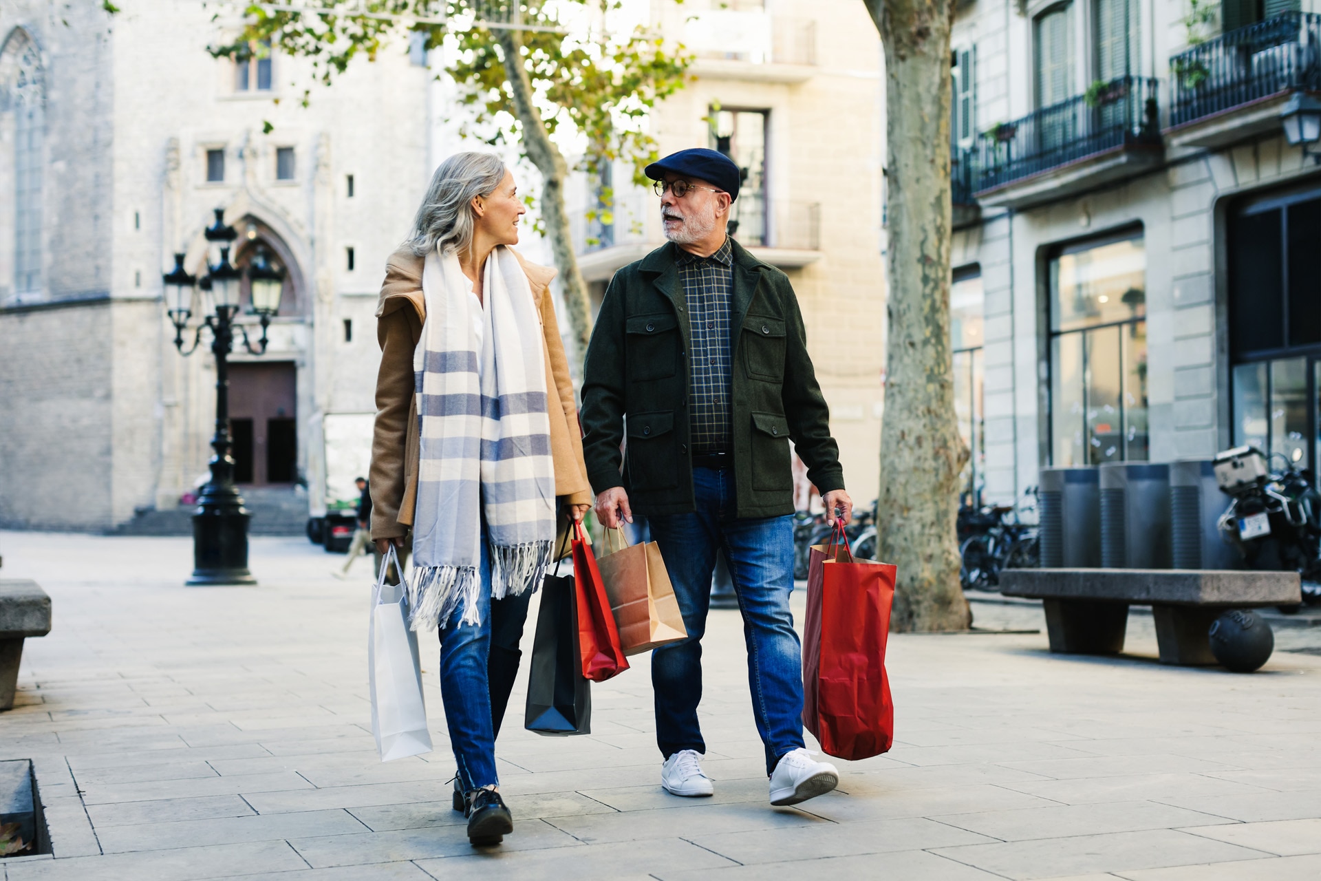 Älteres Paar spaziert mit Einkaufstaschen im Winter eine Straße entlang.