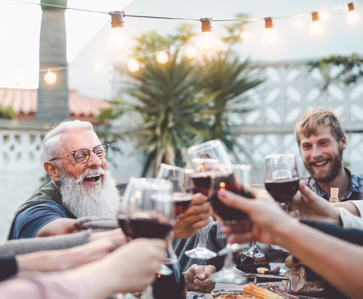 Glückliche Familie beim Abendessen im Garten stößt mit Rotwein an − Menschen verschiedenen Alters und verschiedener Herkunft bei einer fröhlichen Grillparty − Konzept: Eltern, jung und alt, Wochenendaktivität