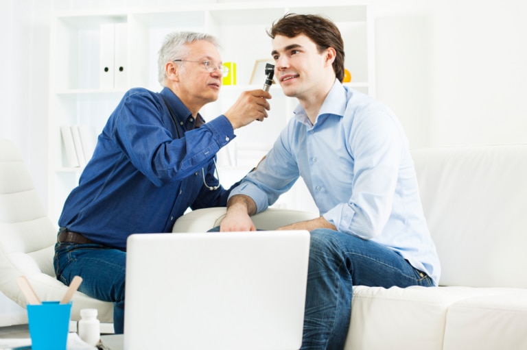 Middle-aged audiologist looking into ear of a young male patient.