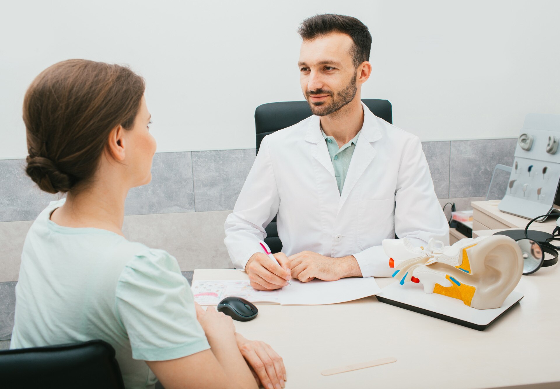 Middle-aged audiologist looking into ear of a young male patient.