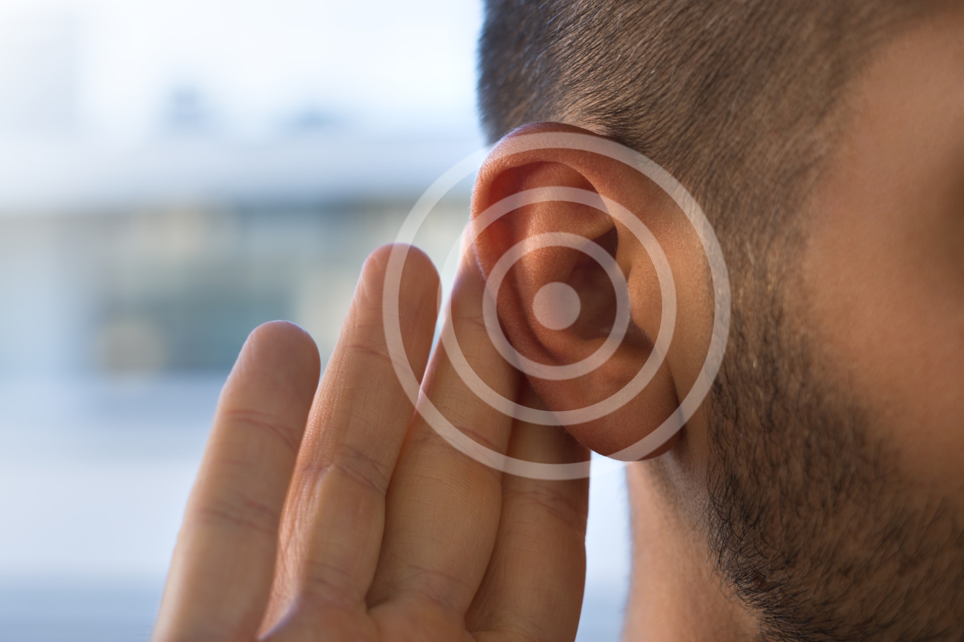 A closeup of a man's ear with a hand touching it, indicating listening.