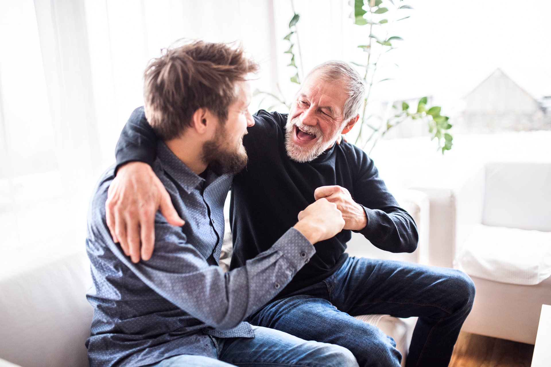 A hipster son sitting on a sofa with his father, both smiling, laughing