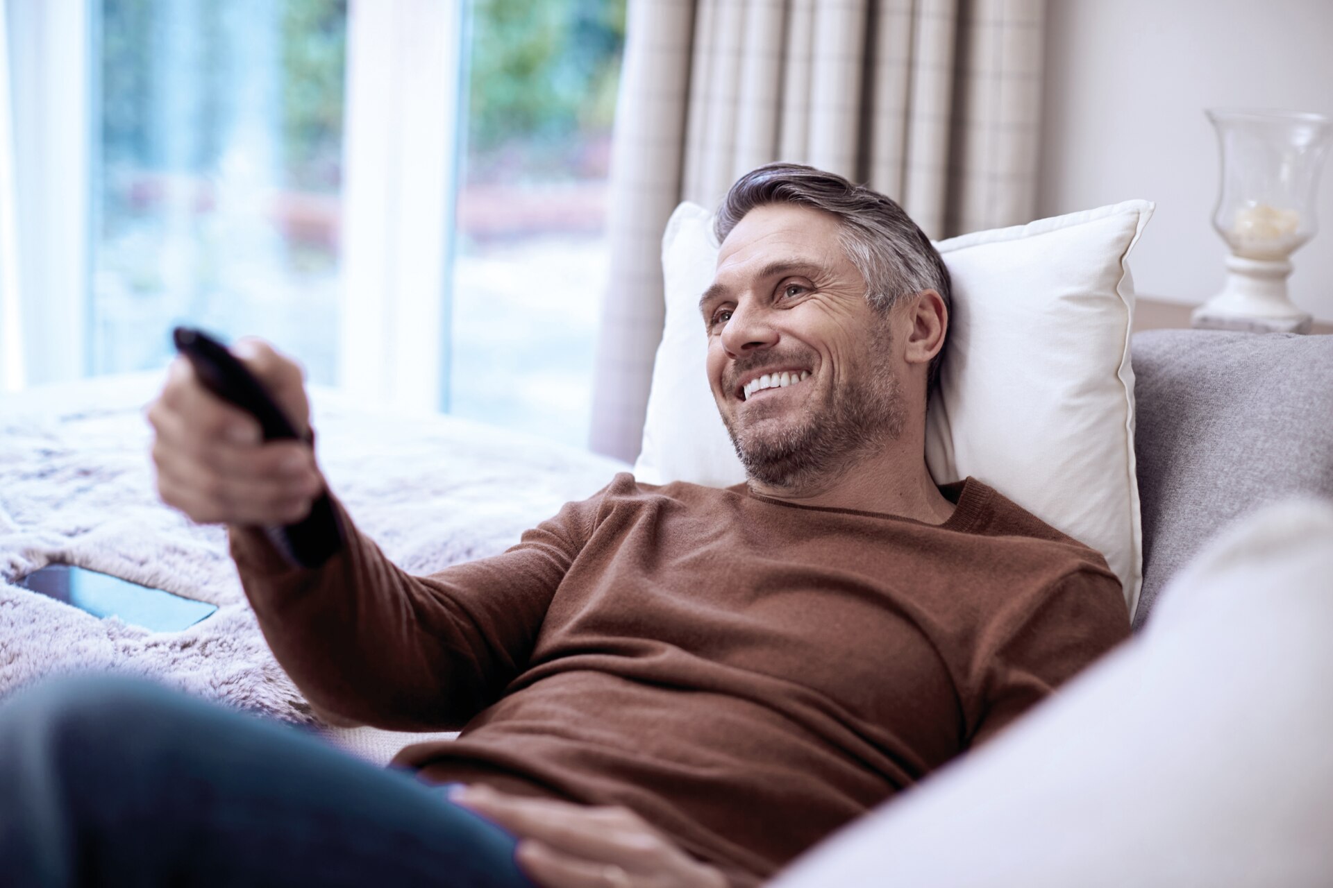 Happy person on the the couch with remote in hand pointing at the tv.