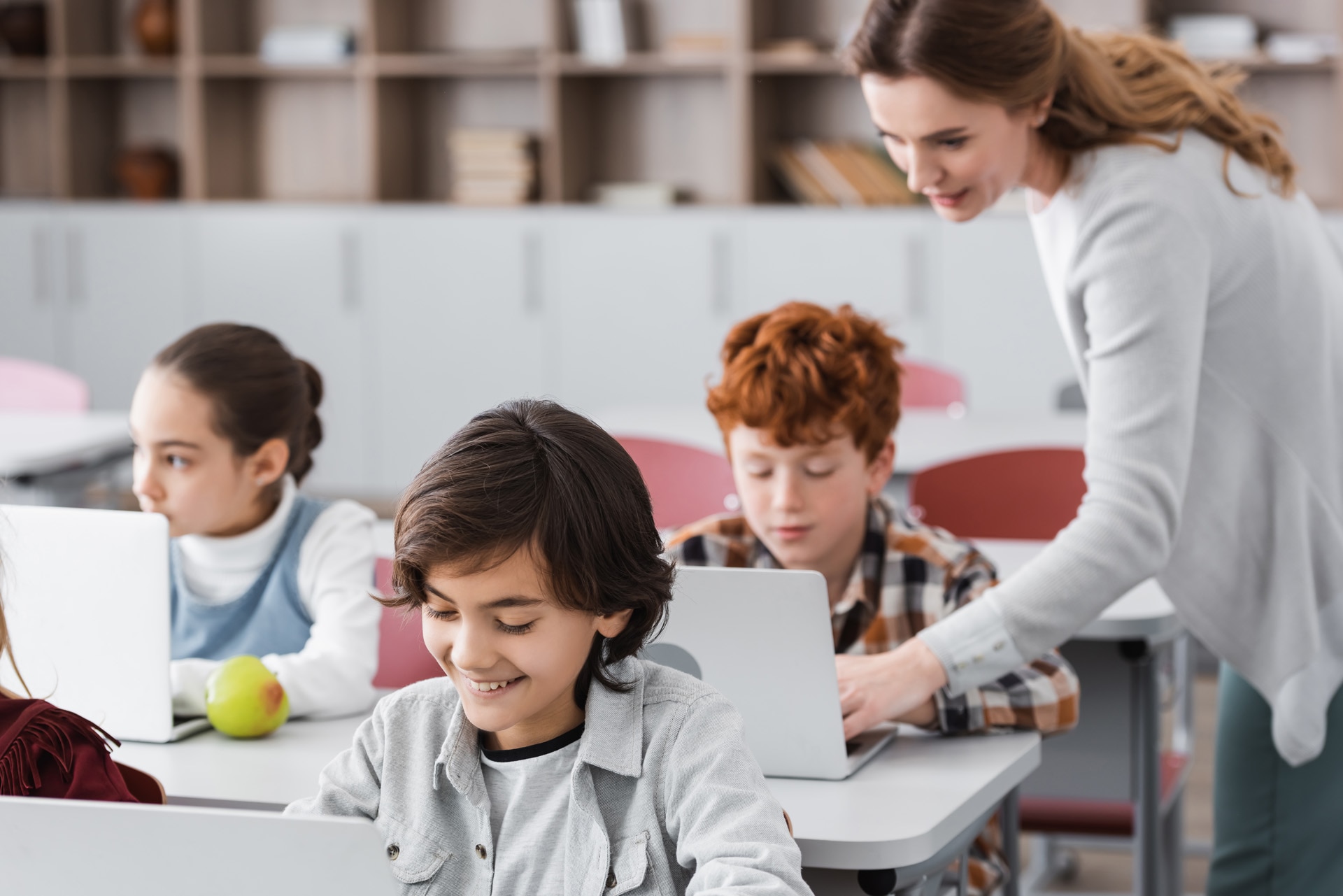 teacher helping schoolboy working on laptop during lesson, blurred background; Shutterstock ID 1933850870; purchase_order: -; job: -; client: -; other: -