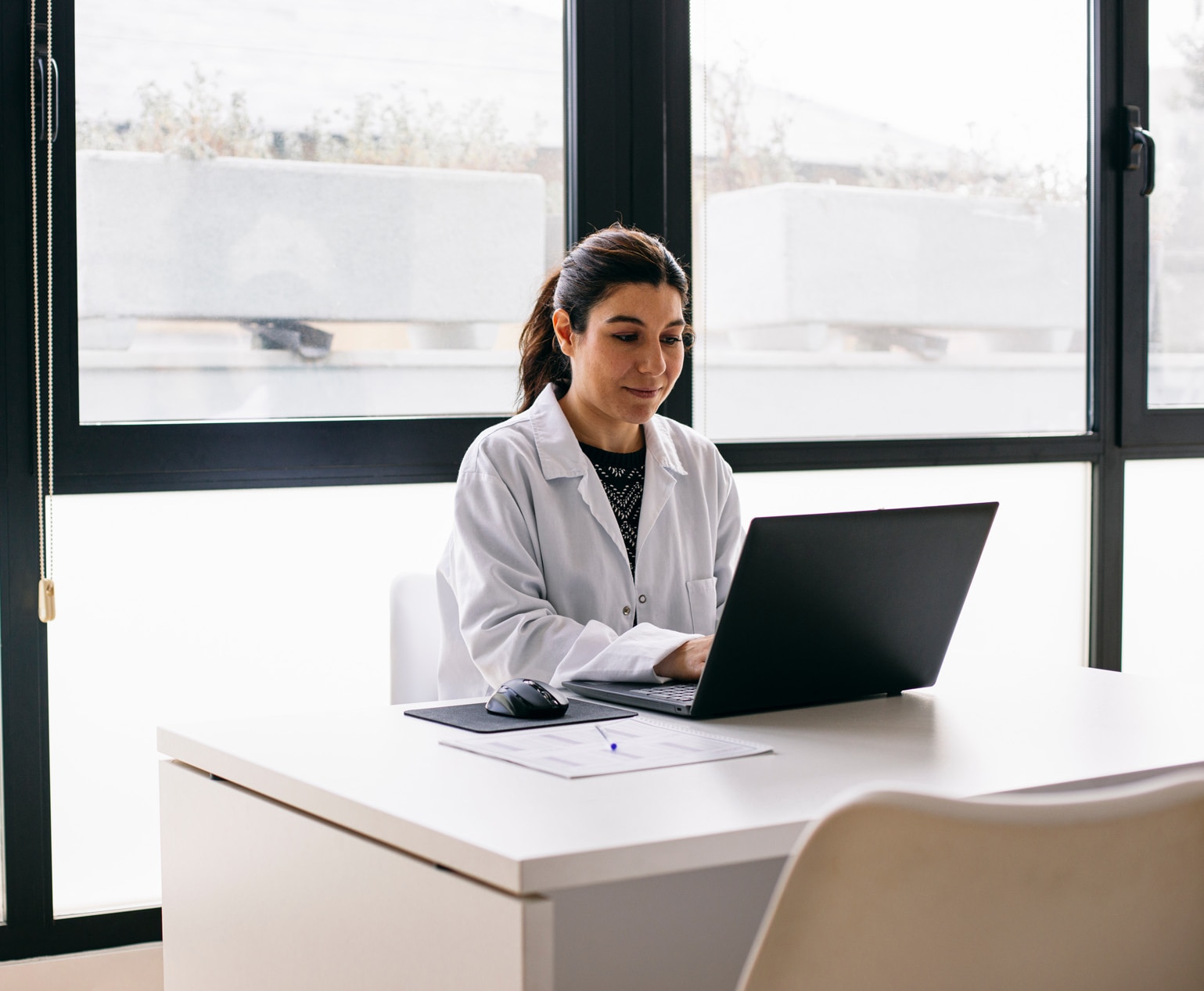 Médecin assise au bureau de son cabinet alors qu’elle utilise un ordinateur portable.