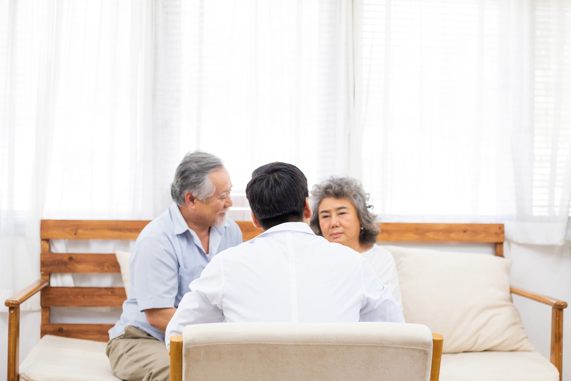 Vista posterior de un médico discutiendo el diagnóstico de los resultados de las pruebas y dando consejos a una pareja de pacientes de edad avanzada en su casa.