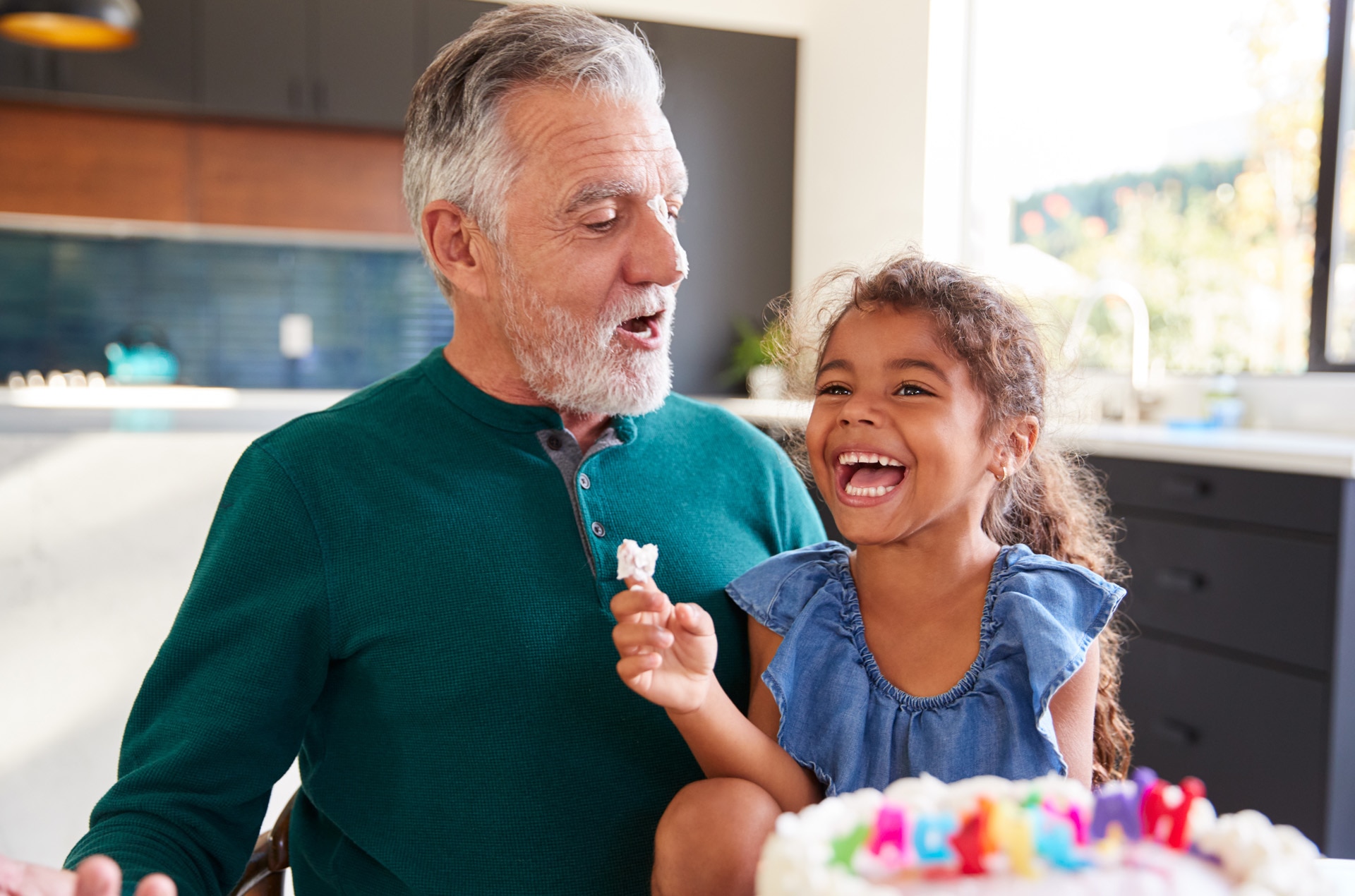 Una nieta celebra un cumpleaños con su abuelo poniéndole crema pastelera en la nariz y riéndose