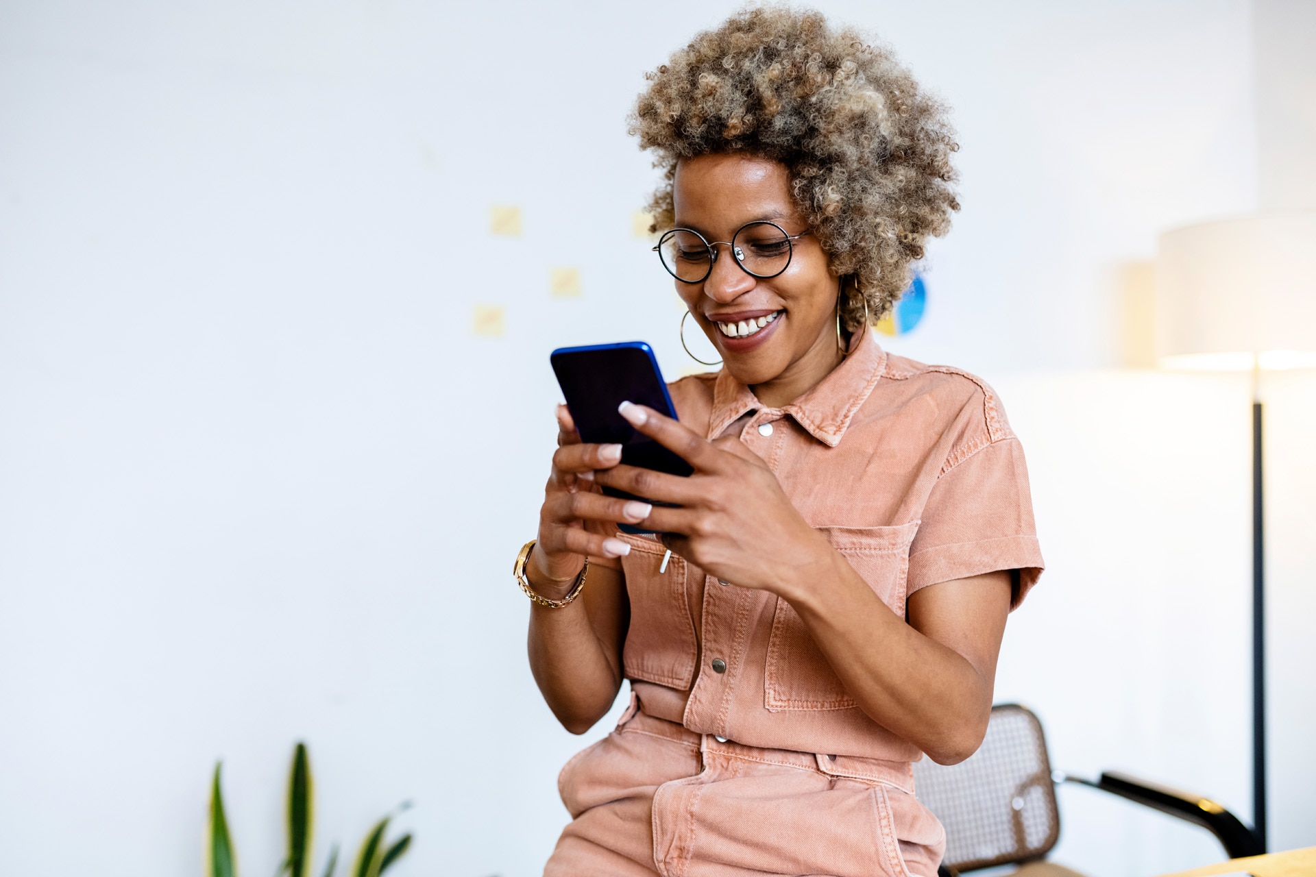 Glimlachende vrouwelijke ondernemer die haar smartphone gebruikt in haar thuiskantoor.