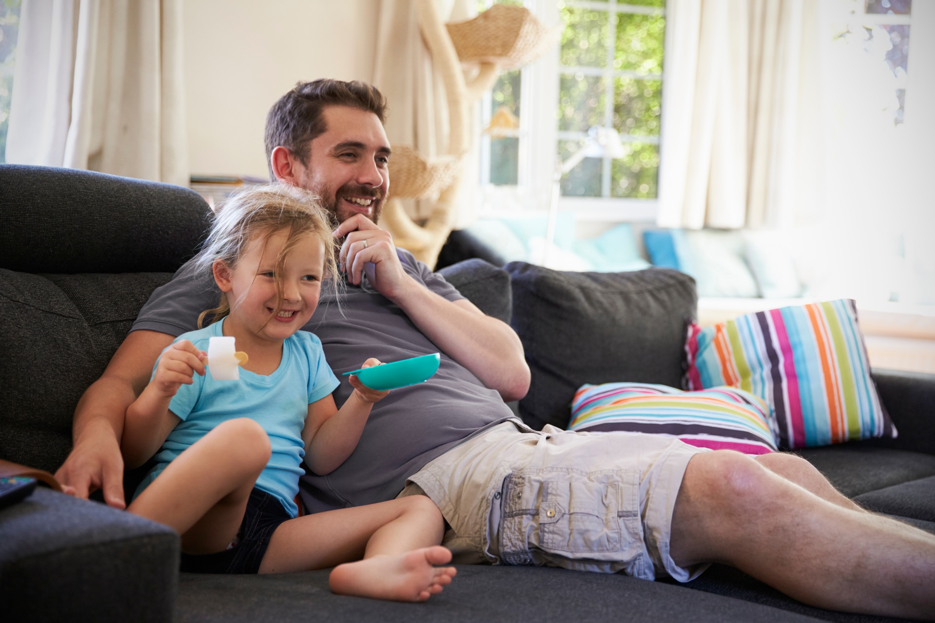 Father and daughter sitting on sofa watching tv together