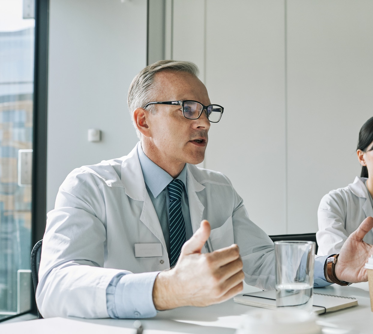 Portrait of mature doctor sitting at meeting table in conference room while speaking during medical seminar