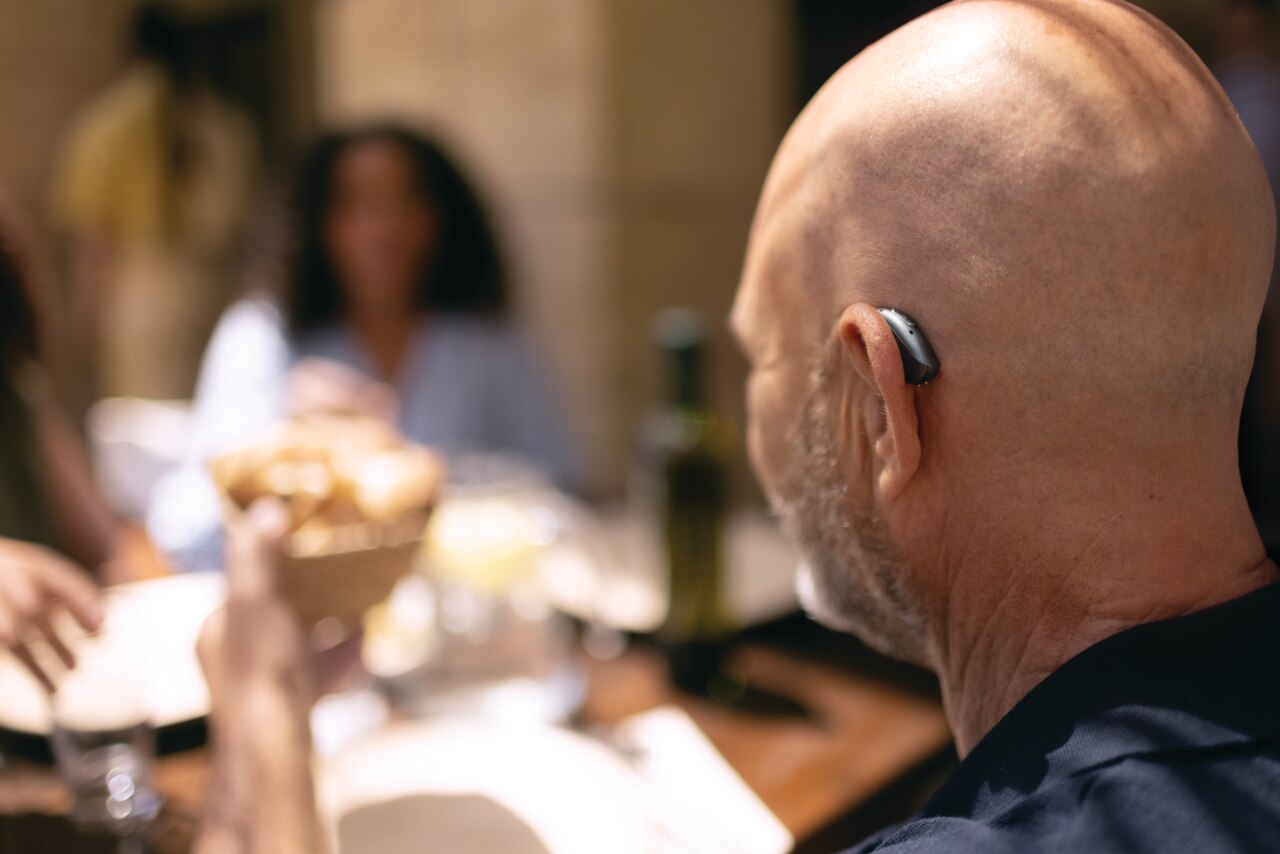Gros plan sur un porteur d'appareil auditif assis � une table de restaurant en plein air Homme avec une aide auditive