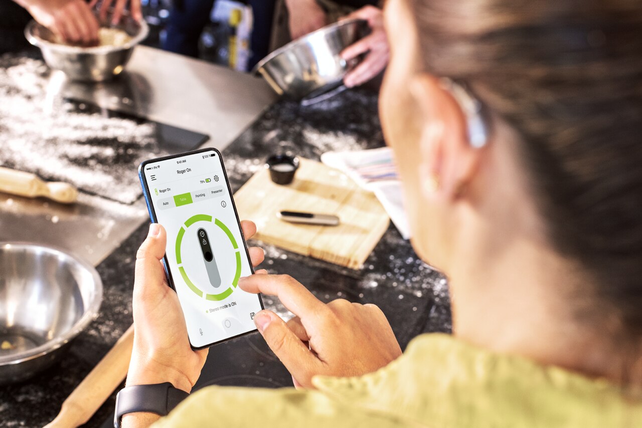 Une femme lors d'un cours de cuisine acc�de � l'application Phonak sur un t�l�phone portable Une femme qui regarde son téléphone