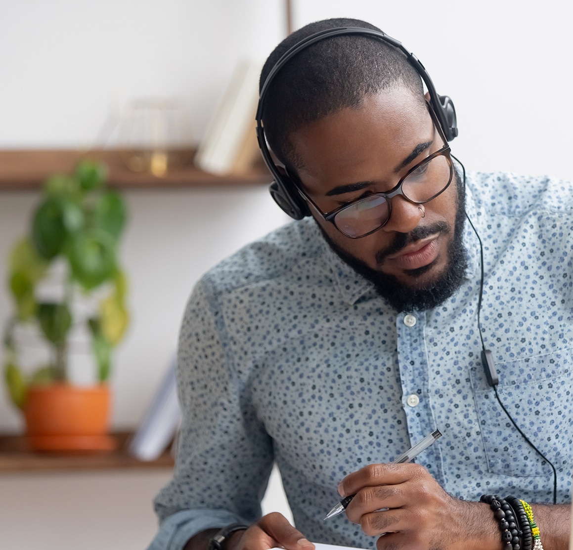 Focused african business man in headphones writing notes in notebook watching webinar video course, serious black male student looking at laptop listening lecture study online on computer e learning