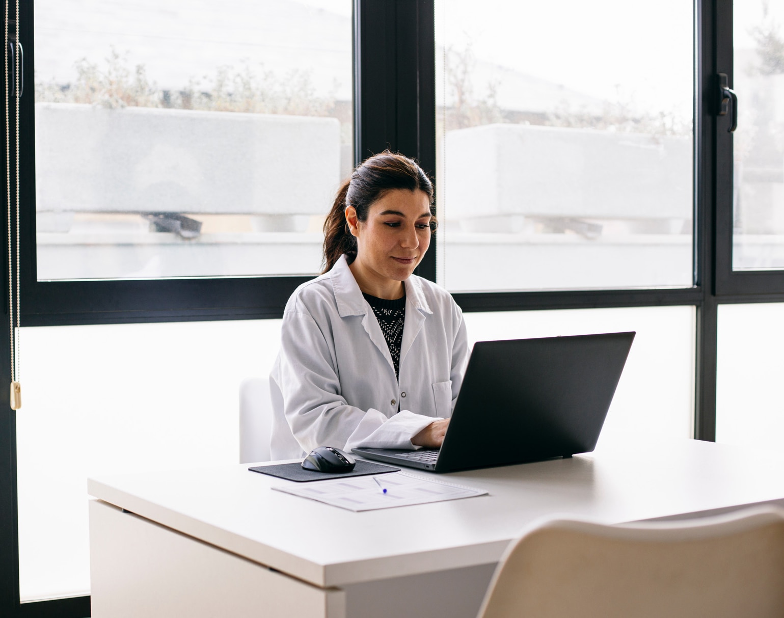 Ärztin sitzt am Schreibtisch vor einem Laptop in einer Arztpraxis.