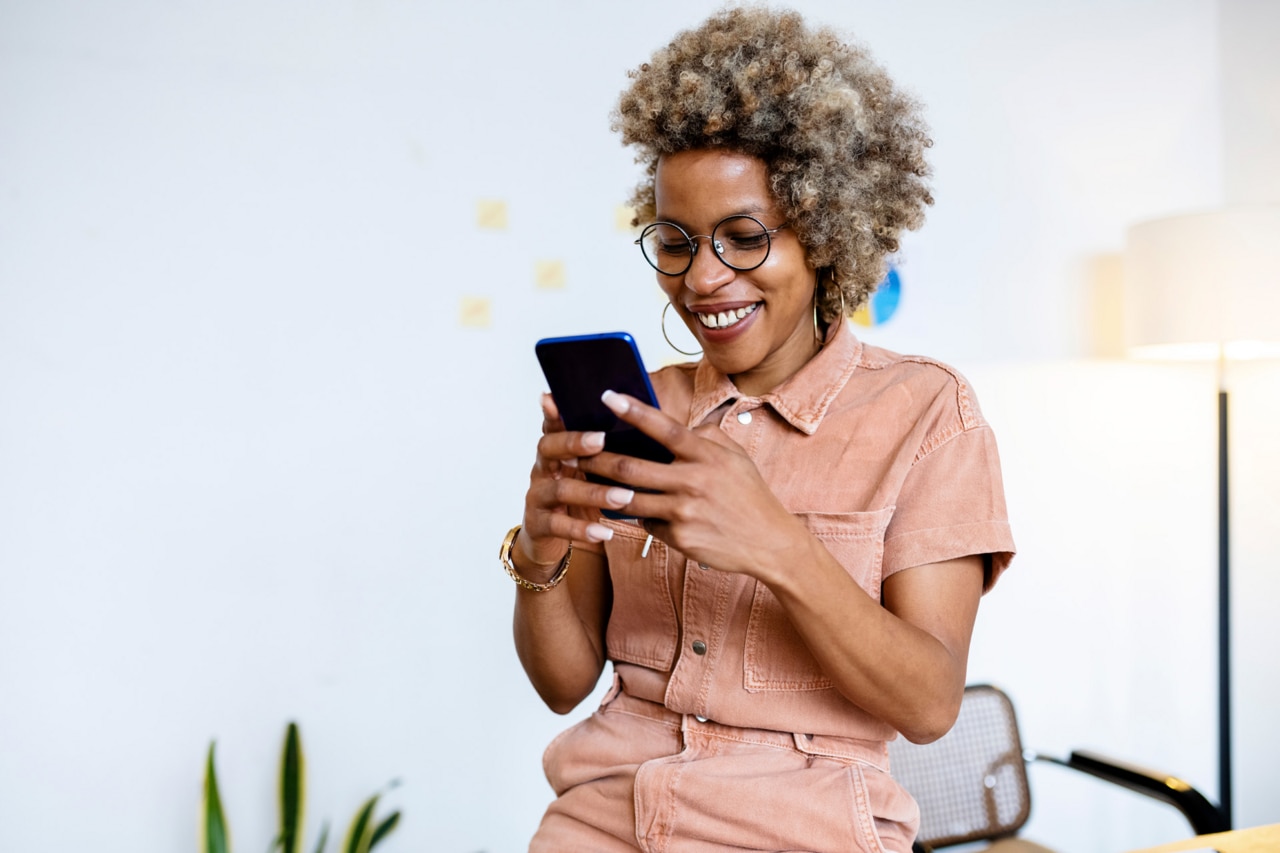 Smiling female entrepreneur using smart phone at home office