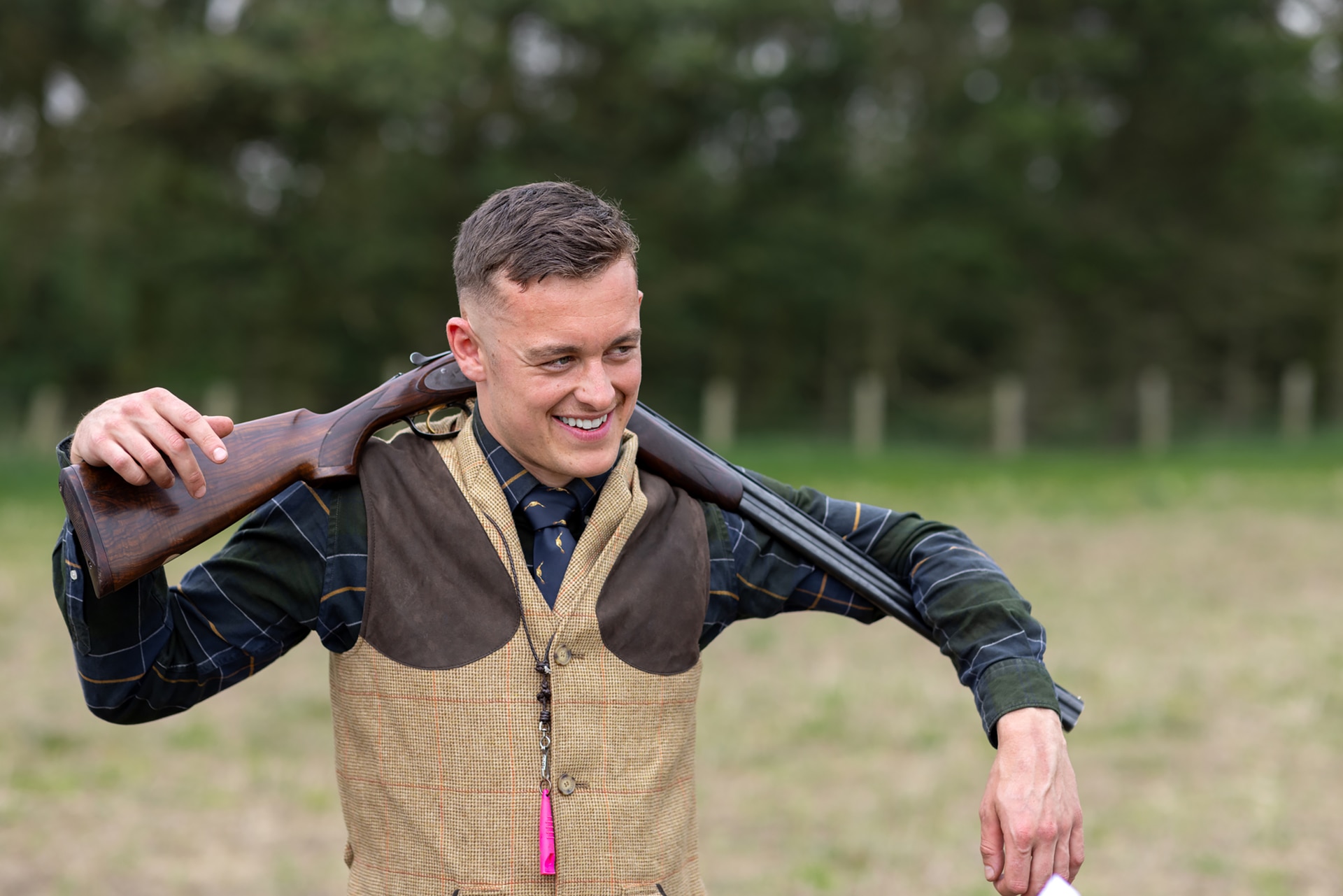 2156177734 Nahaufnahme eines jungen Mannes, der mit einer geöffneten Schrotflinte um den Hals steht. Er ruht beide Arme auf der Schrotflinte. Der Mann trägt traditionelle englische Jagdbekleidung.