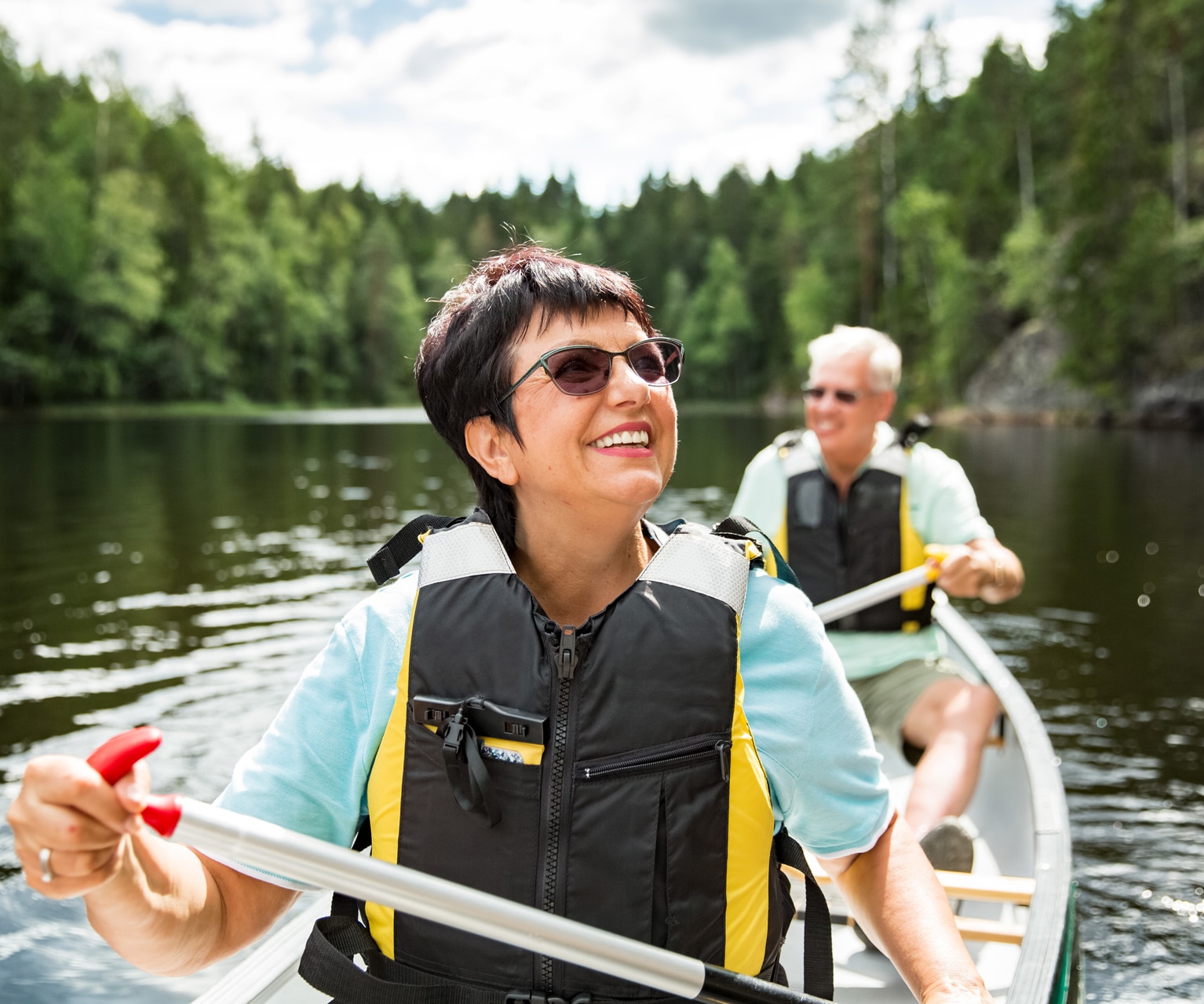 Glückliches älteres Paar in Schwimmwesten fährt Kanu auf einem Waldsee. Sonniger Sommertag. Touristen auf einer Abenteuerreise in Finnland.