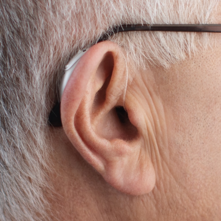 Close-up of older person's ear with receiver-in-the-canal hearing aid.