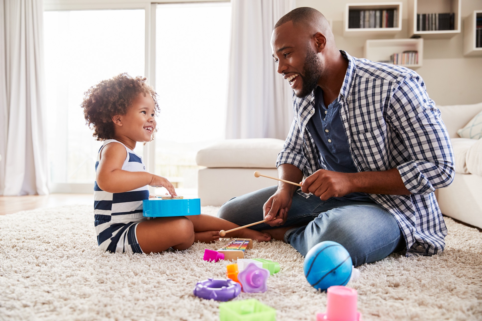 Jeune père jouant avec sa petite fille sur des instruments de musique basiques, scène intérieure.