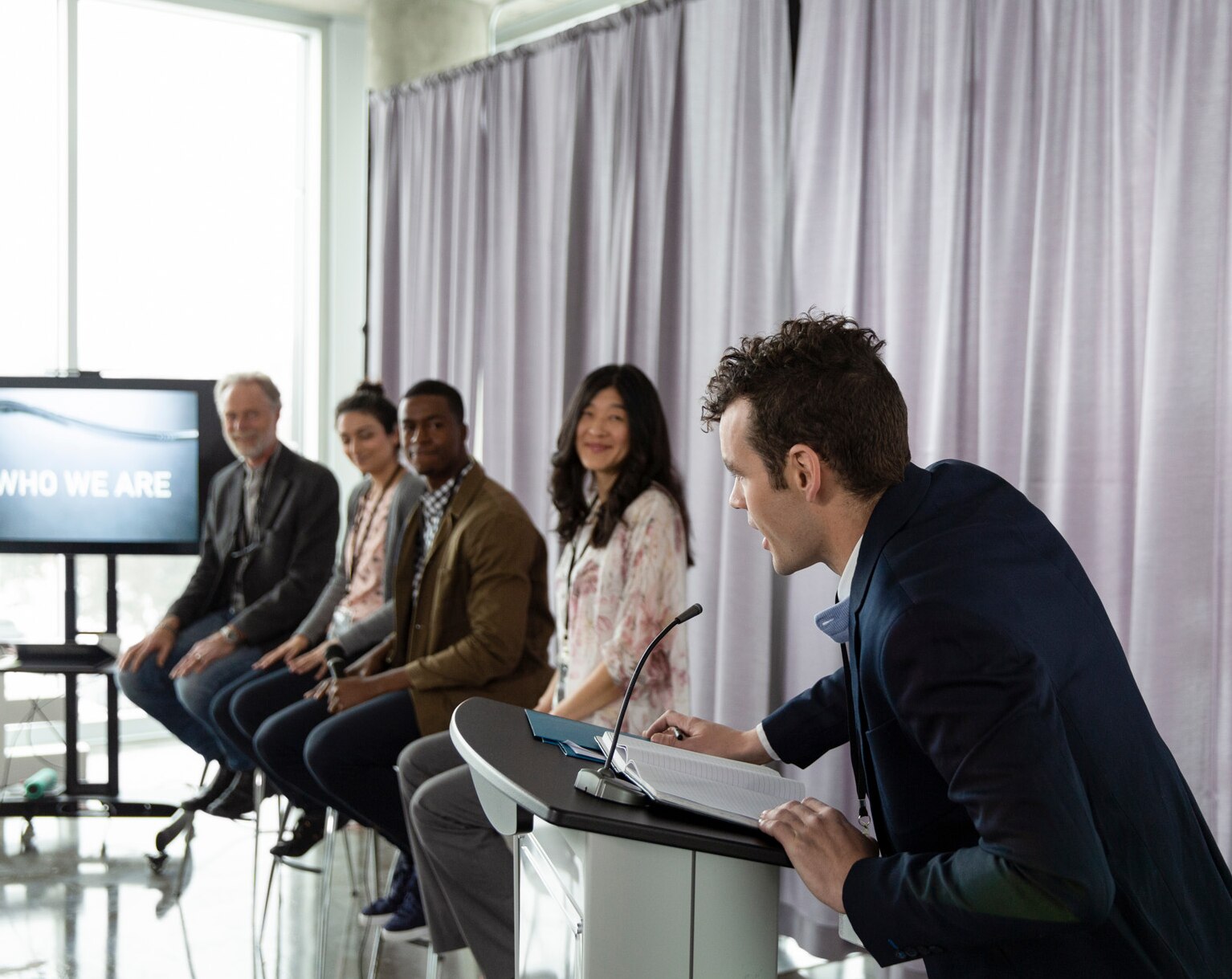 Man at podium introducing panel of motivation speakers at conference