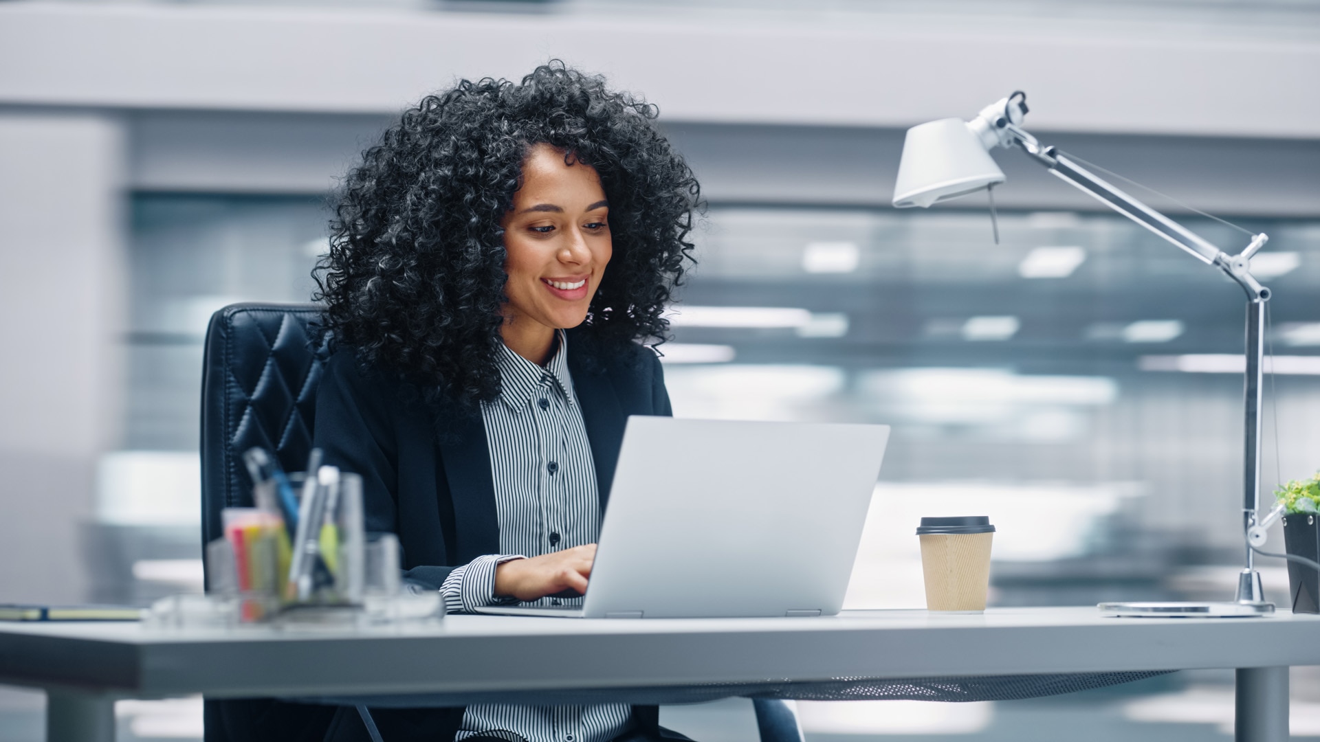 Modern Office: Black Businesswoman Sitting at Her Desk Working on a Laptop Computer. Smiling Successful African American Woman working with Big Data e-Commerce. Motion Blur Background; Shutterstock ID 2109768191; purchase_order: -; job: -; client: -; other: -