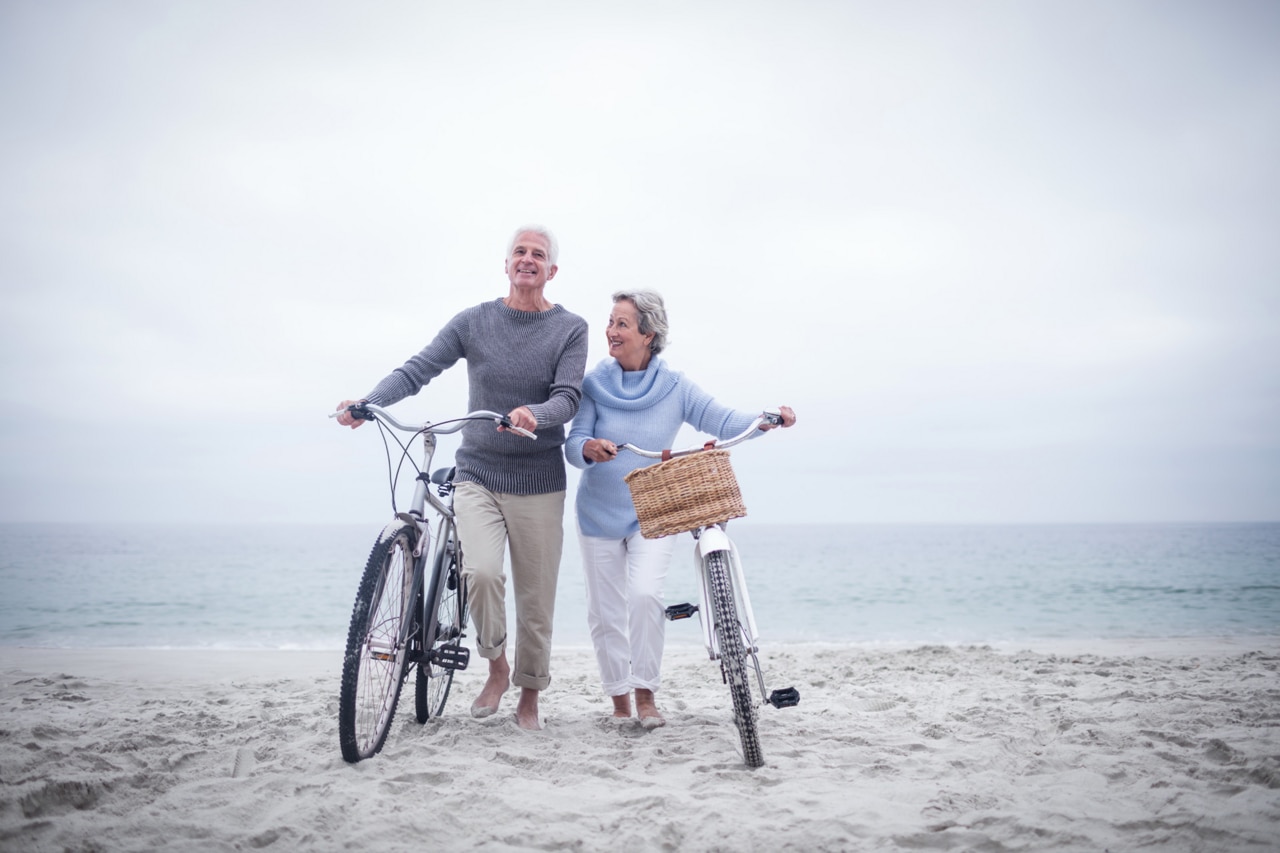 Couple de personnes âgées en train de faire du vélo sur la plage.