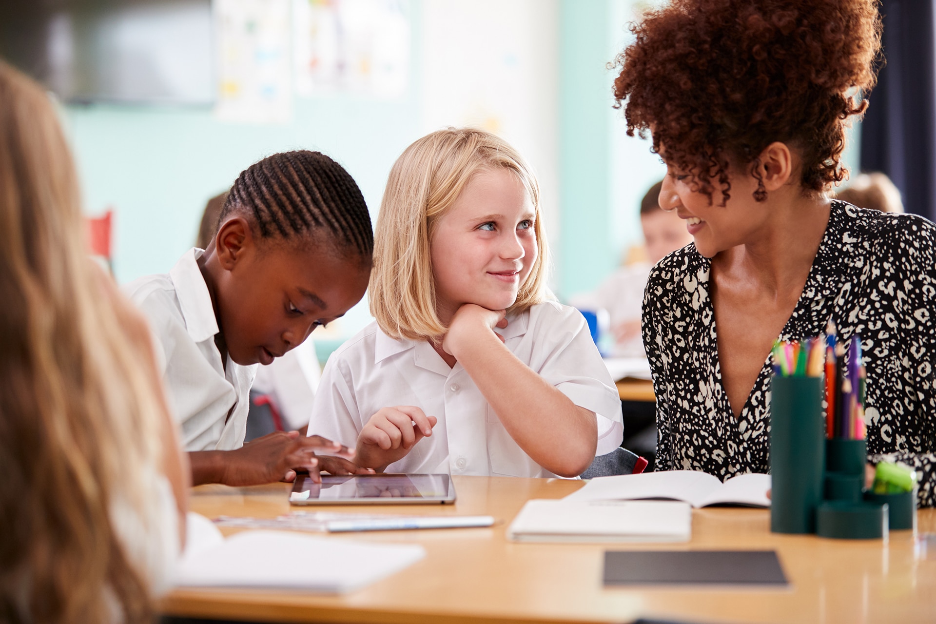 Enseignante avec deux élèves du primaire portant l'uniforme à l'aide d'une tablette numérique au bureau