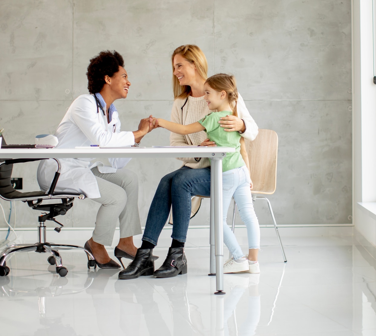 Cute little girl with her mother at the pediatrician examination by African american female doctor