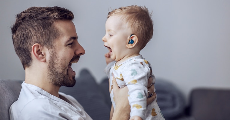 Young father with an infant wearing a hearing aid.