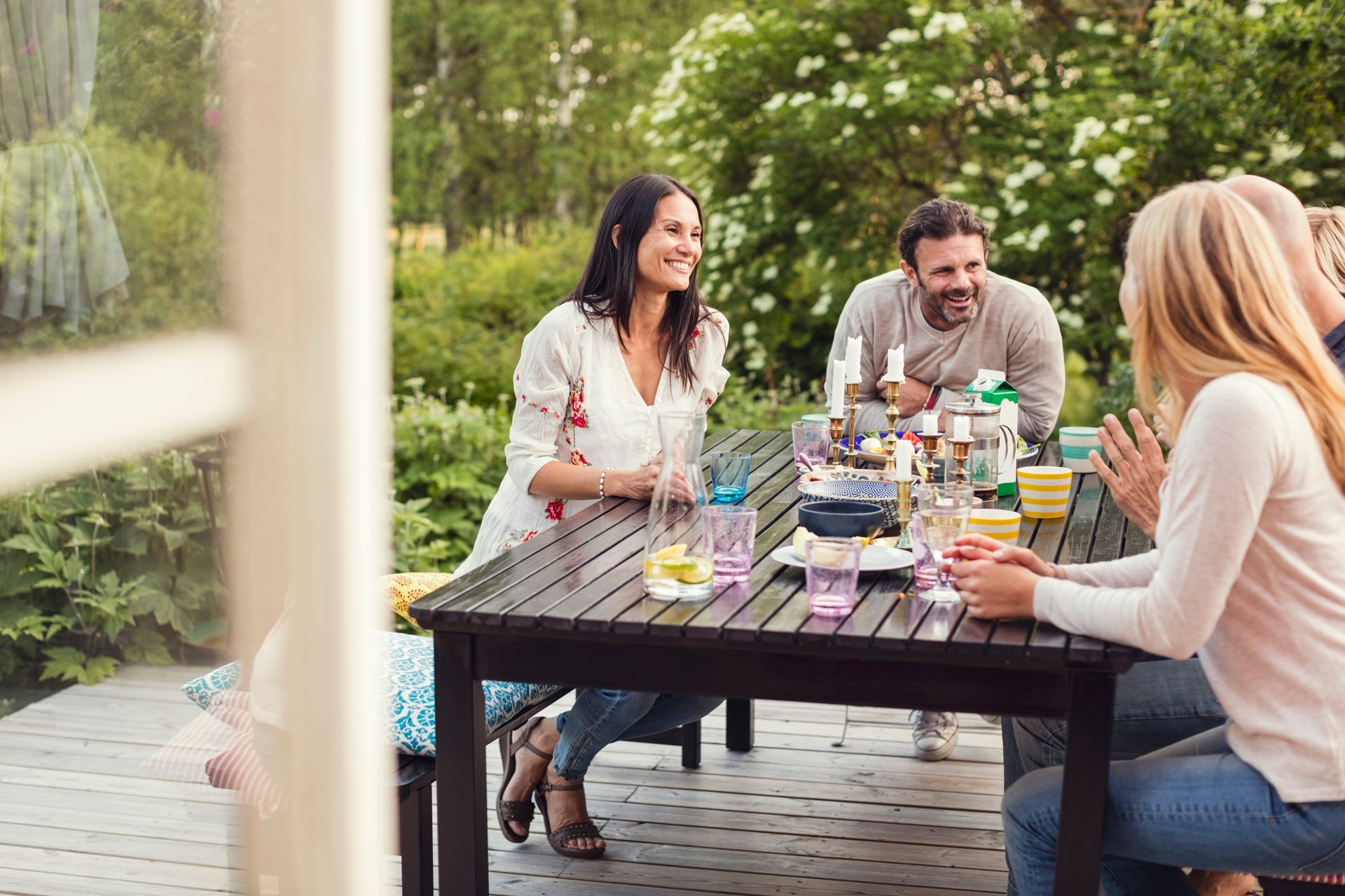 Glad familie og ven sidder sammen ved et spisebord i baggården
