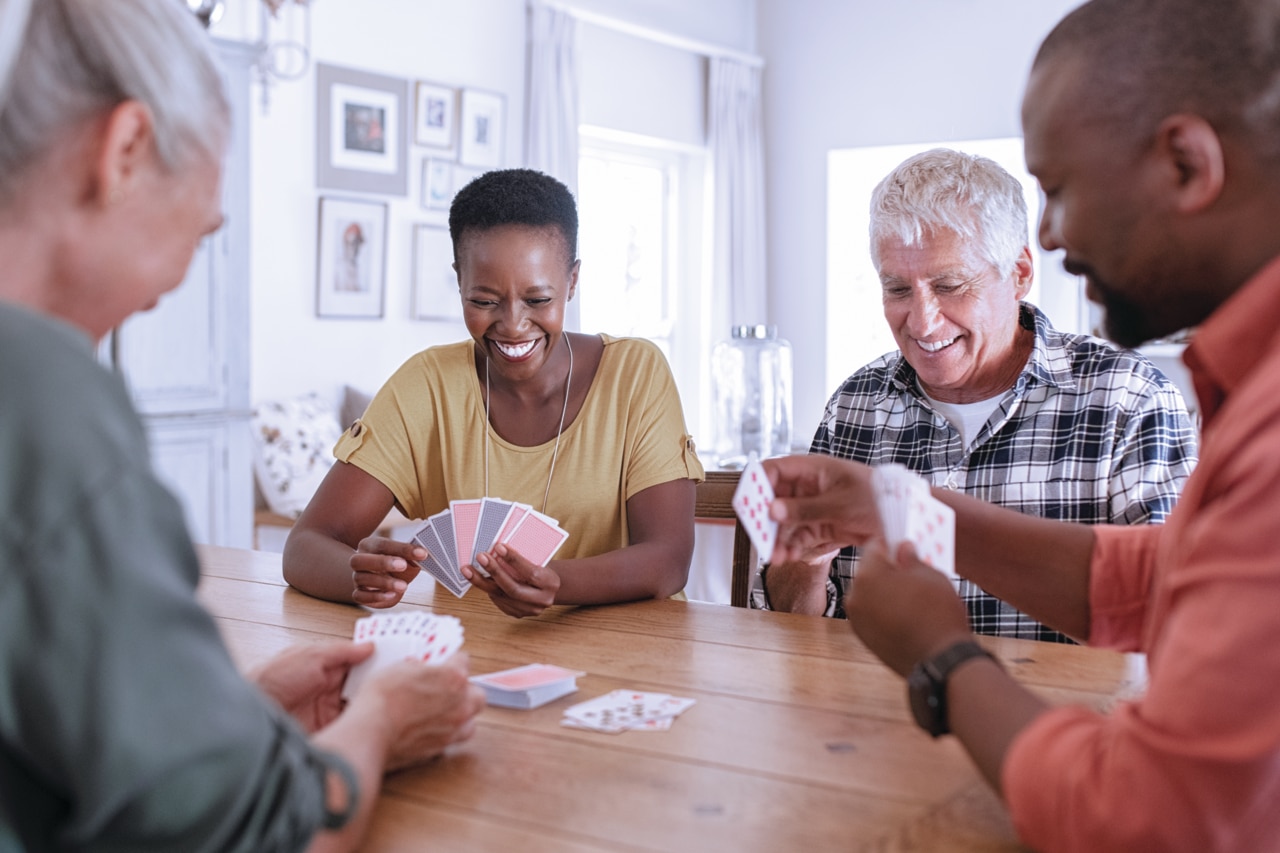 Retired multiethnic people playing cards together at home. Happy senior friends with african couple playing cards. Cheerful active seniors playing game at lunch table.