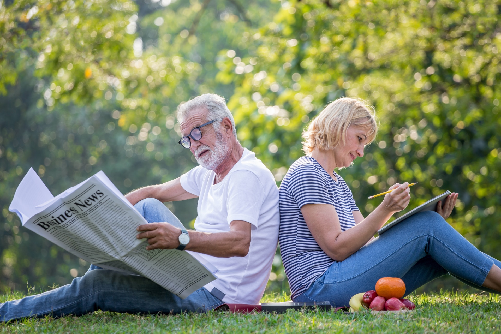Feliz pareja de ancianos relajándose sentada espalda con espalda en el parque leyendo el periódico y tomando notas para escribir el diario juntos. ancianos en el parque de verano. Ancianos descansando. Relaciones maduras.