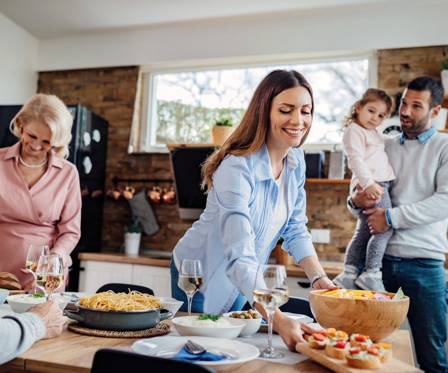 Young happy woman setting dining table for multigenerational family lunch at home.