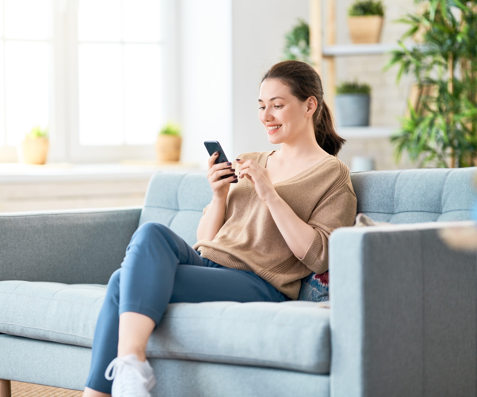 Happy casual beautiful woman is talking on a phone sitting on a sofa at home.