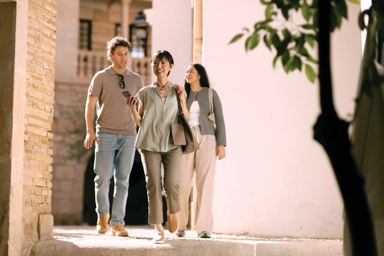 Un groupe de personnes se promenant dans une vieille ville, une femme tenant un t�l�phone � la main, v�rifiant la navigation. �t�, soleil Aide auditive Phonak Audéo Infinio