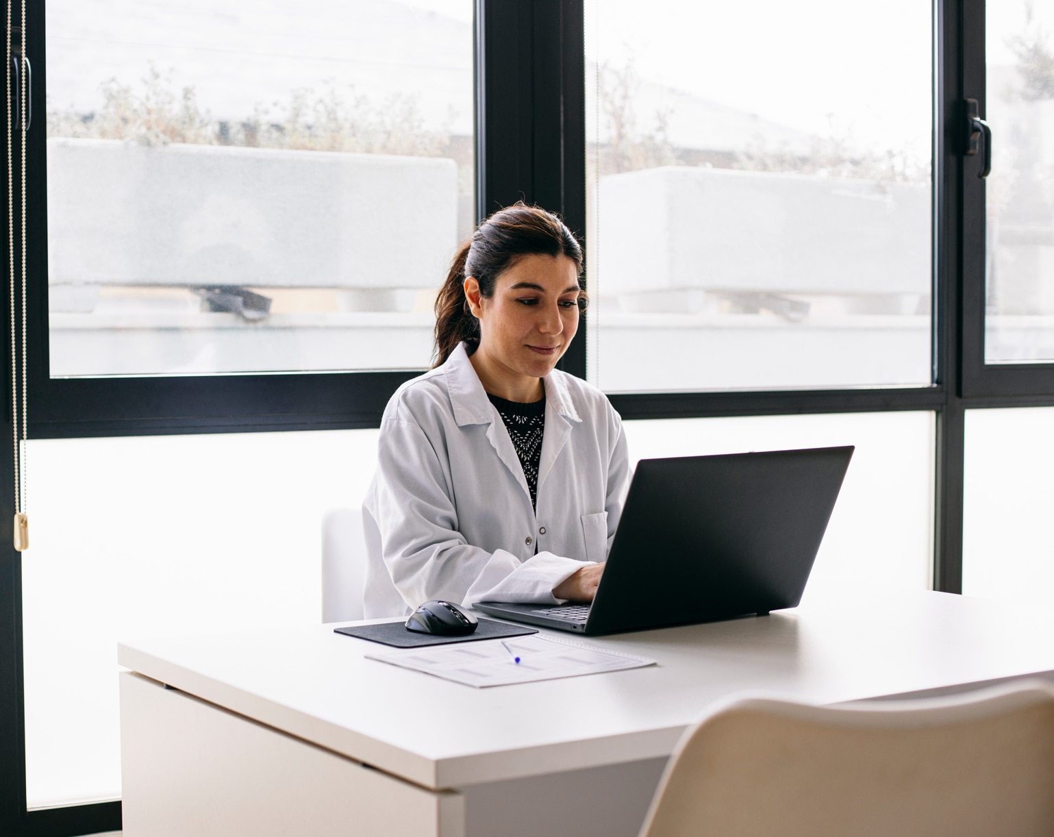 Médecin assise au bureau de son cabinet alors qu’elle utilise un ordinateur portable.