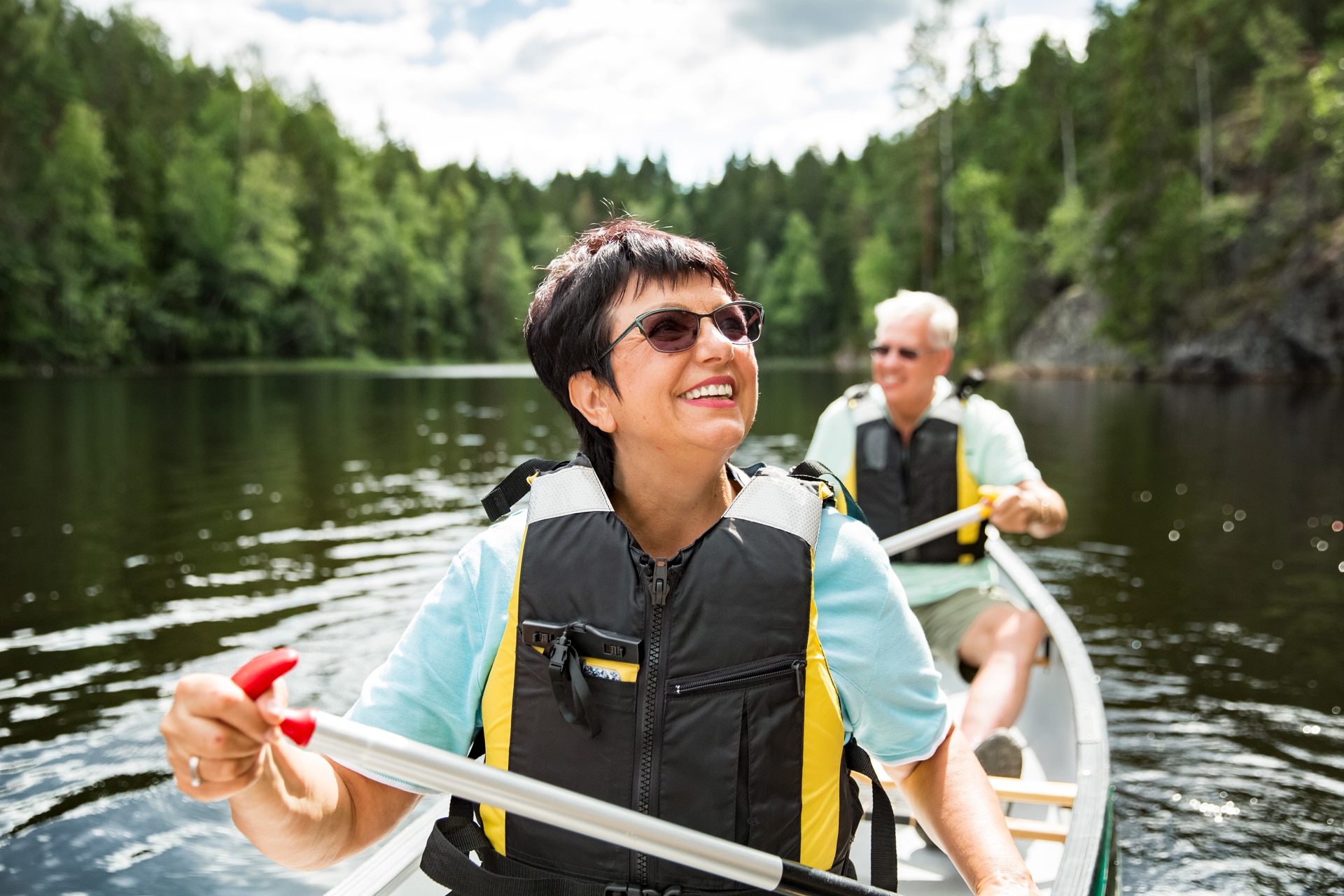 Happy mature couple in life vests canoeing in forest lake. Sunny summer day. Tourists traveling in Finland, having adventure. ; Shutterstock ID 1947633676; purchase_order: -; job: -; client: -; other: -