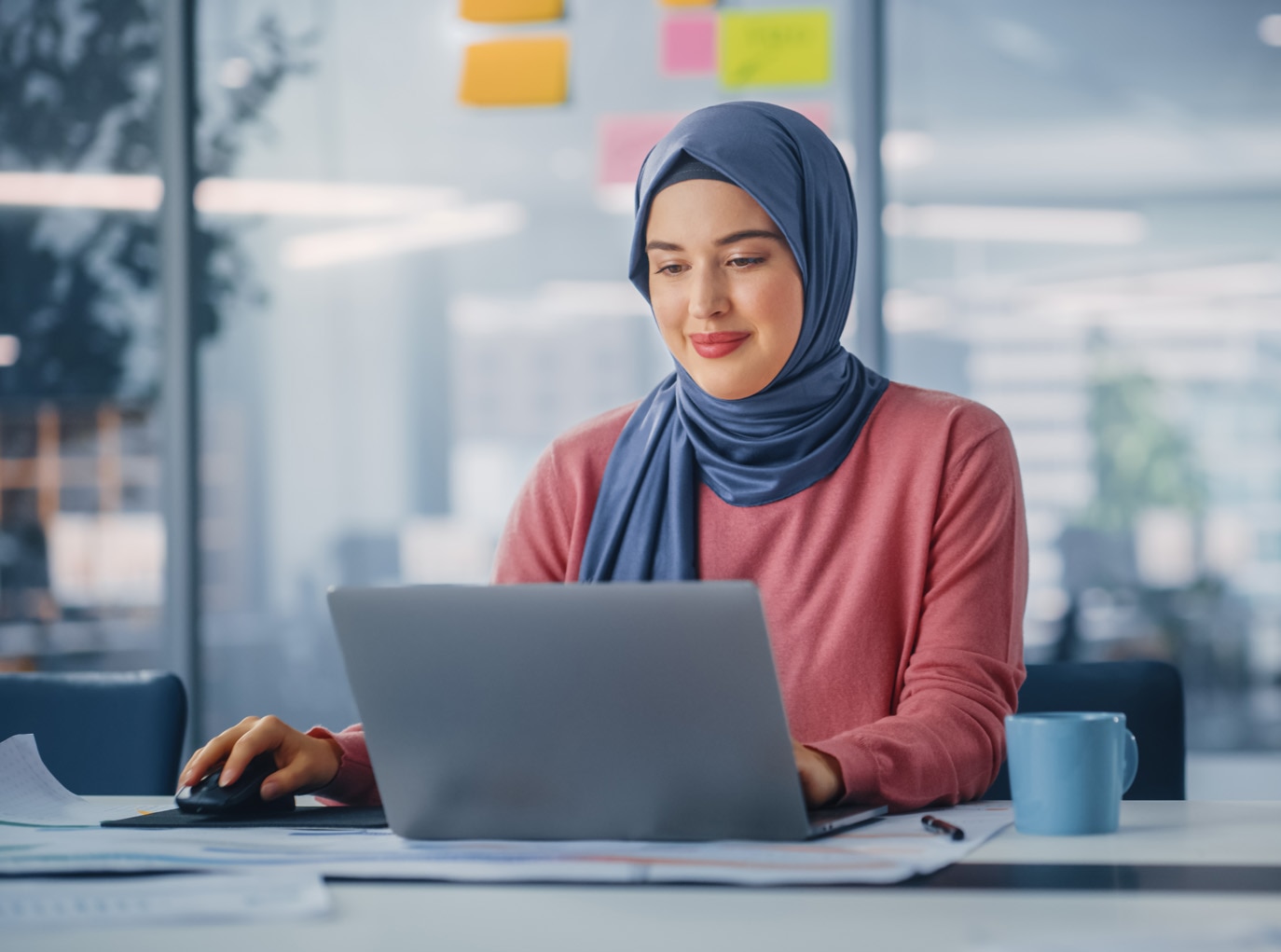 Bureau moderne : Portrait d'une jeune femme d'affaires musulmane portant le hijab travaille sur un ordinateur portable, effectue l'analyse de données, la conception de sites Web, le développement créatif.