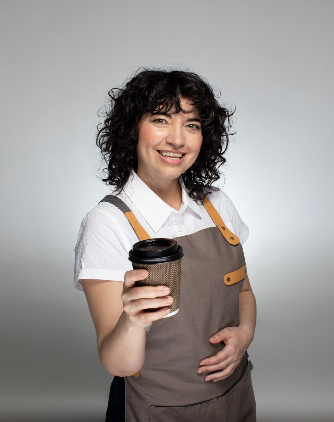 Smiling female barista standing with a big cup of coffee in her hand.