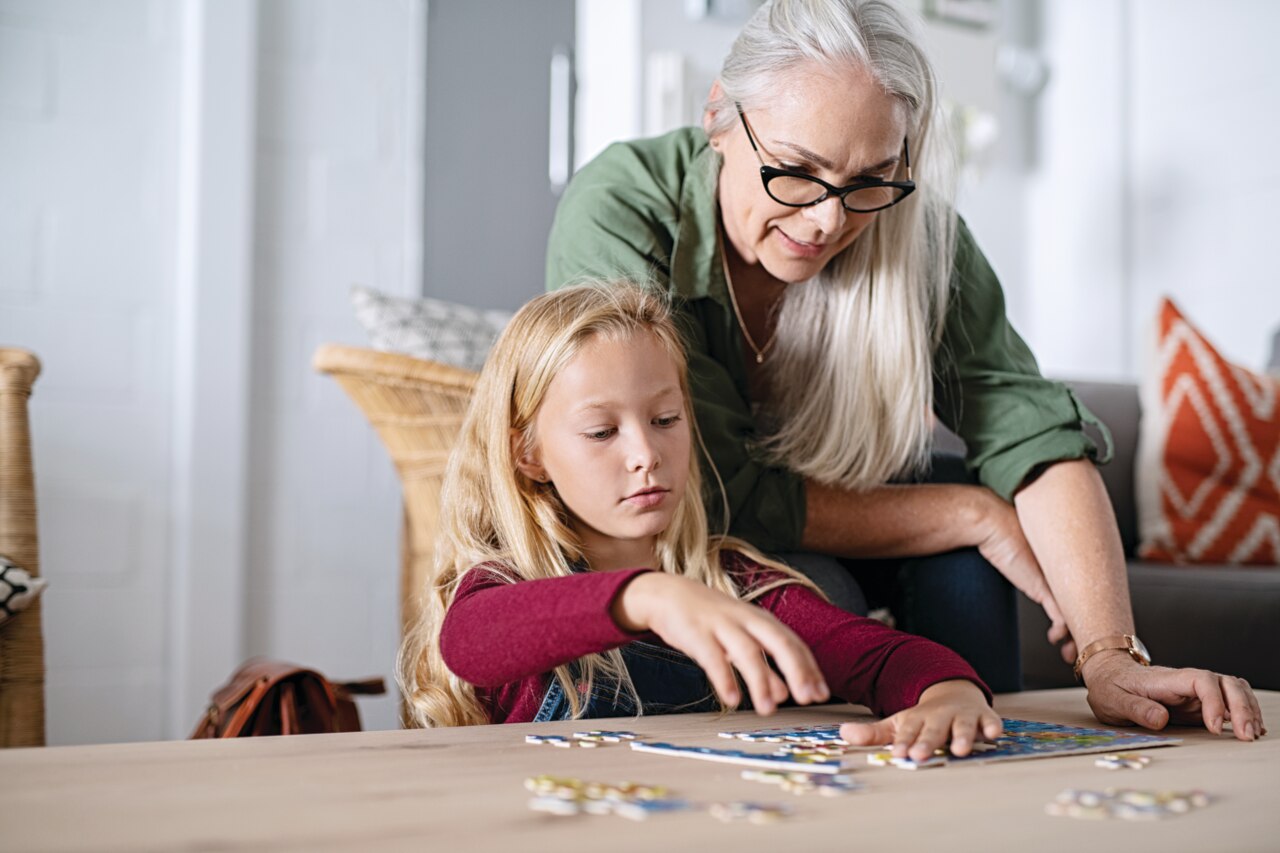 Concentrated little girl doing jigsaw puzzle with old grandmother at home. Cute little granddaughter playing puzzle at the table with senior granny. Smart child assembling pieces with mature woman.; Shutterstock ID 1451181902; purchase_order: Cost Center; job: 600873; other: Phonak