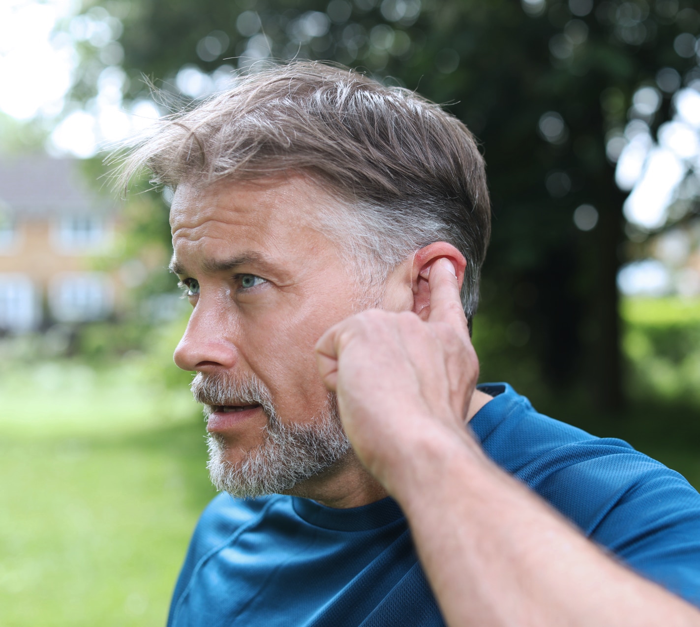 A man out for a jog taps on his left hearing aid to answer a call.